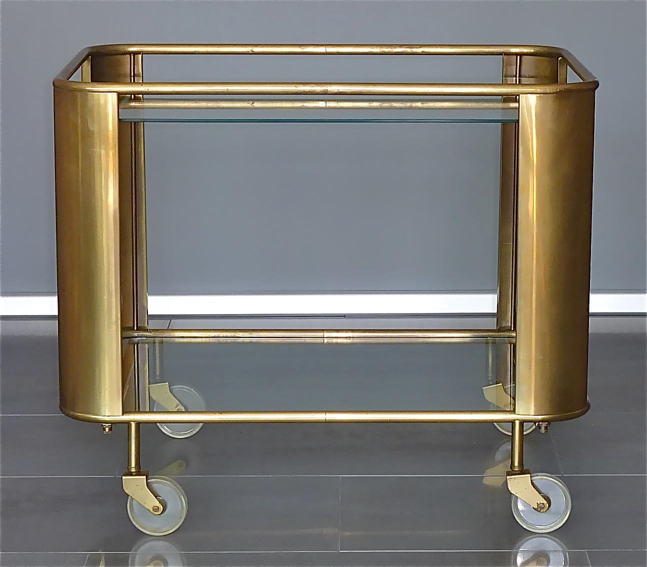 Great vintage modernist Bauhaus / Art Deco bar cart, drinks or serving table trolley on four wheels designed and executed in the 1930s to 1950s in Germany or France. The cool streamline model is made of patinated brass metal, has two glass tiers and