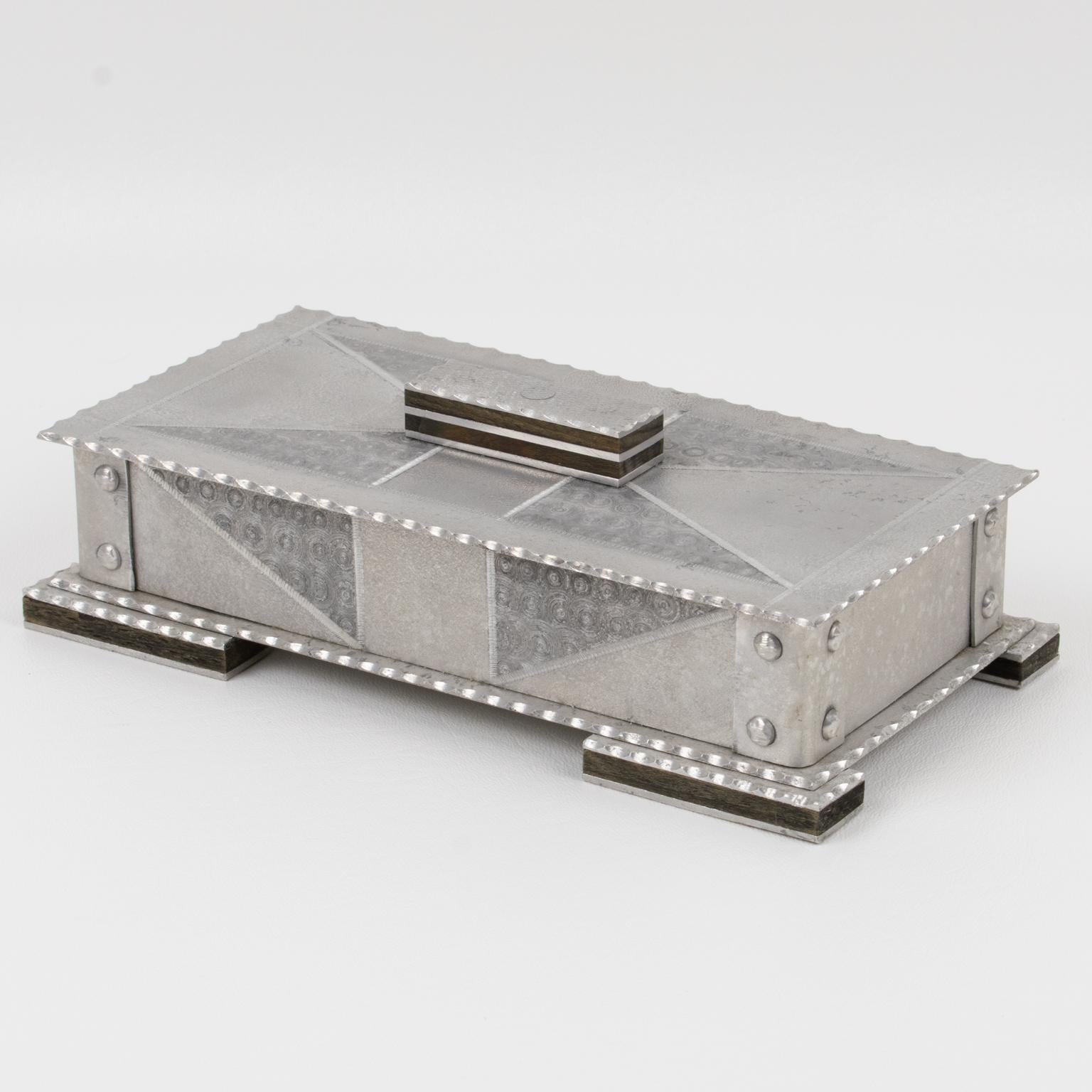 Se trata de una impresionante caja decorativa de aluminio, de principios del siglo XX. El diseño presenta detalles de madera y una forma industrial modernista tipo Bauhaus, Arts & Crafts. Es una gran construcción rectangular con un dibujo geométrico