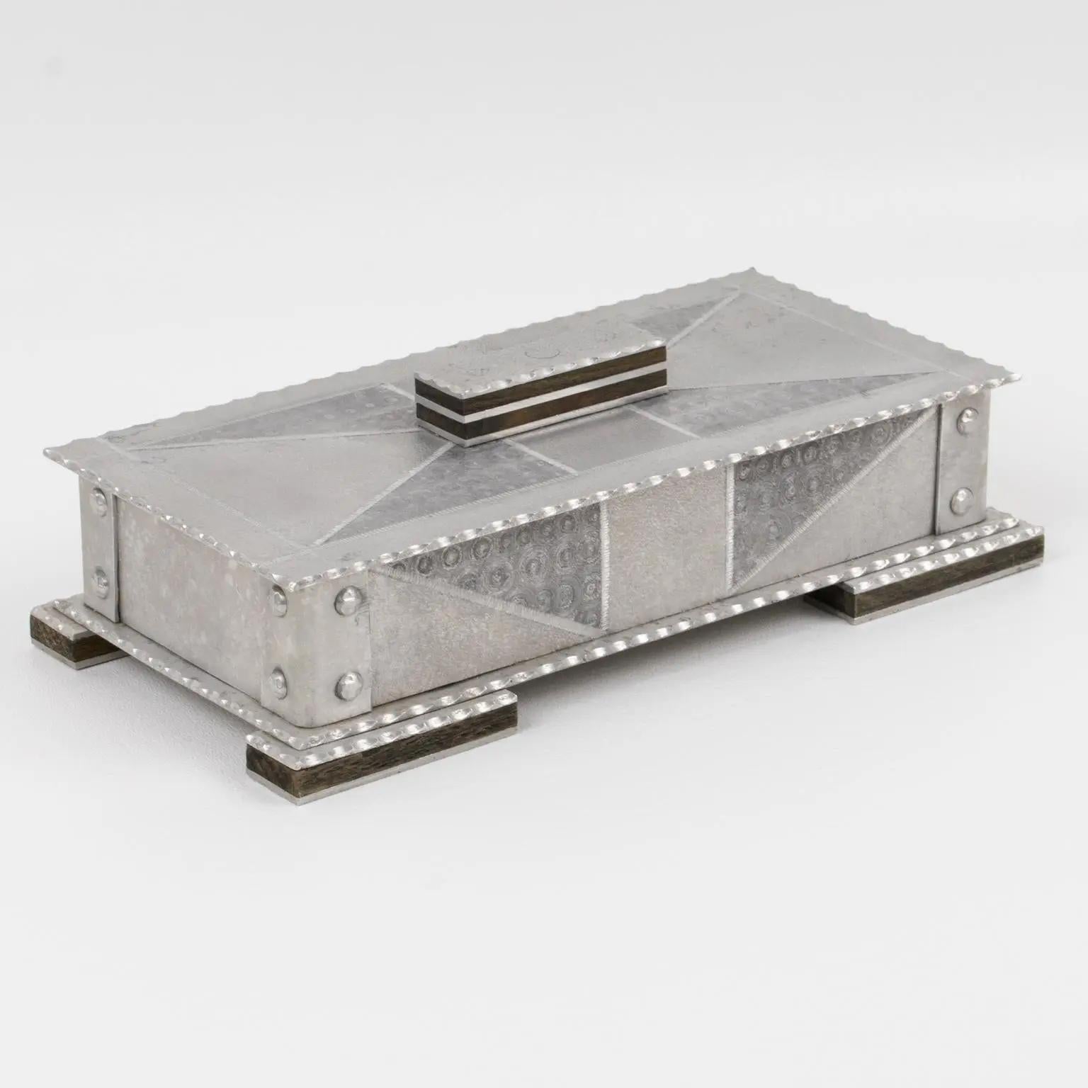 This is a stunning decorative aluminum box from the early 20th century. The design boasts wood detailing and a modernist industrial Bauhaus or Arts & Crafts shape. It is a large rectangular shape with a geometric textured pattern on it. The box is