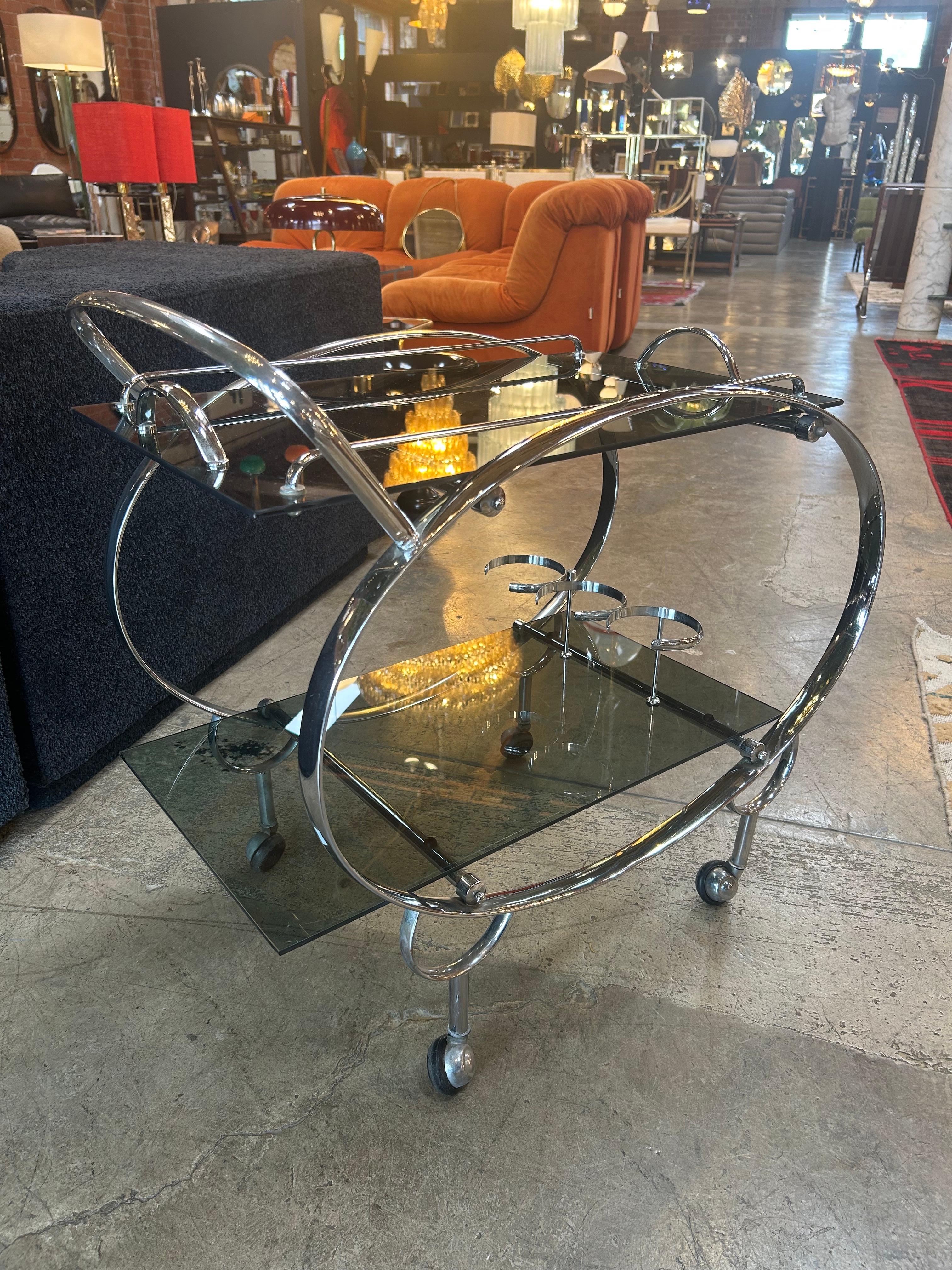 Fabricado en la década de 1930-1940, este carrito de bar Bauhaus de Italia presenta un impresionante diseño Art Déco. Fabricada con elegante metal cromado y estantes de cristal, incluye asas, elegantes curvas y una llamativa forma escultórica. La