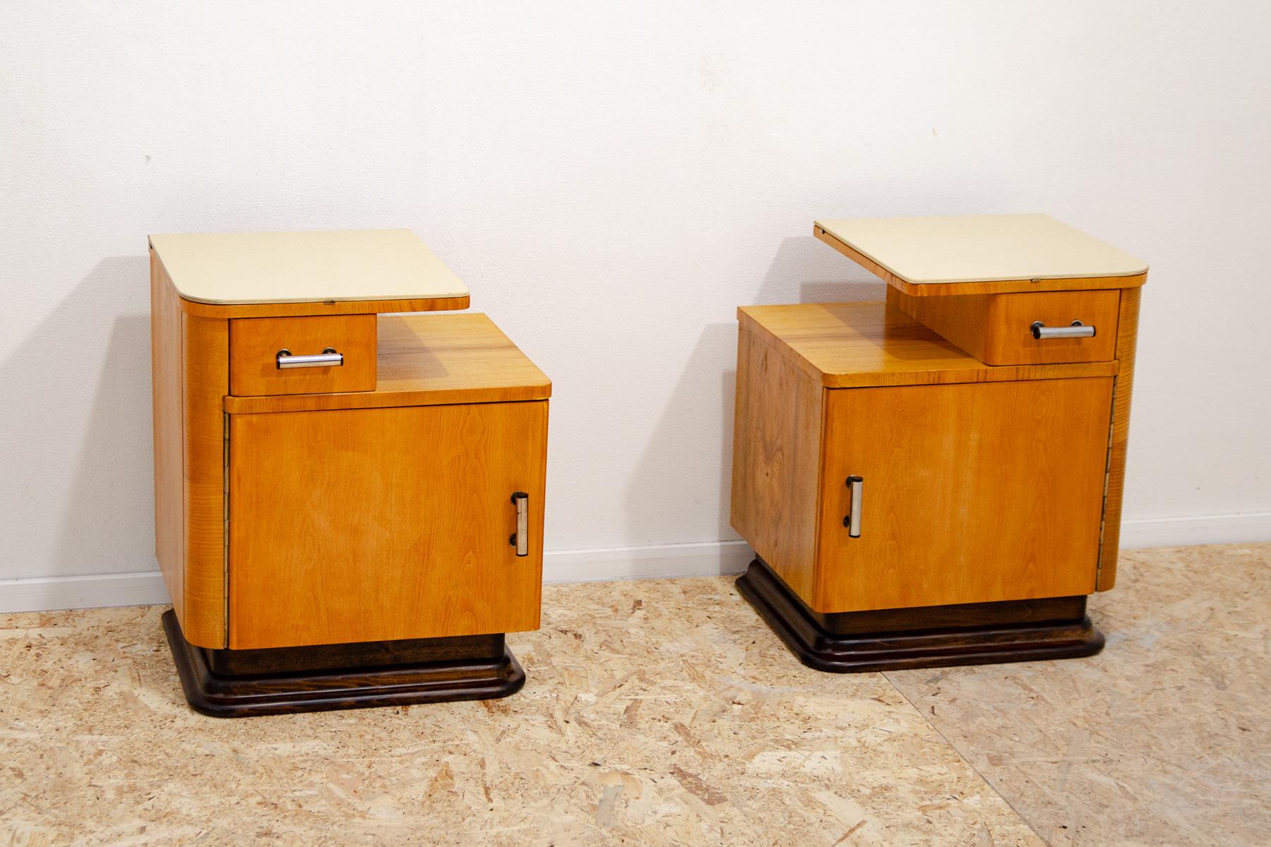 These bedside tables were designed by Jindřich Halabala and made in the 1930s. They are made of beech wood, have chrome handles, and a glass top. There is a solid walnut base on the bottom of the tables. They are in excellent condition, after