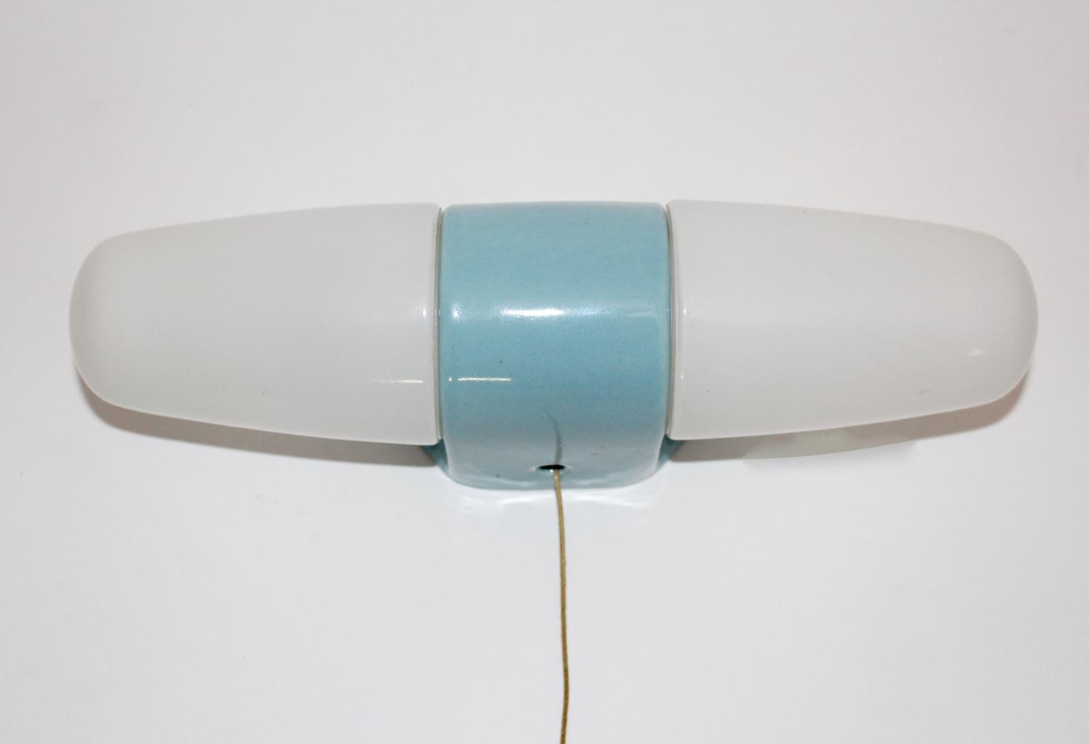 This presented sconce or wall light was planned to use it above a mirror.
It was designed by Wilhelm Wagenfeld and produced by Lindner, Germany, circa 1956.
Also the sconce was made of light blue porcelain with two E 14 sockets and two opaline