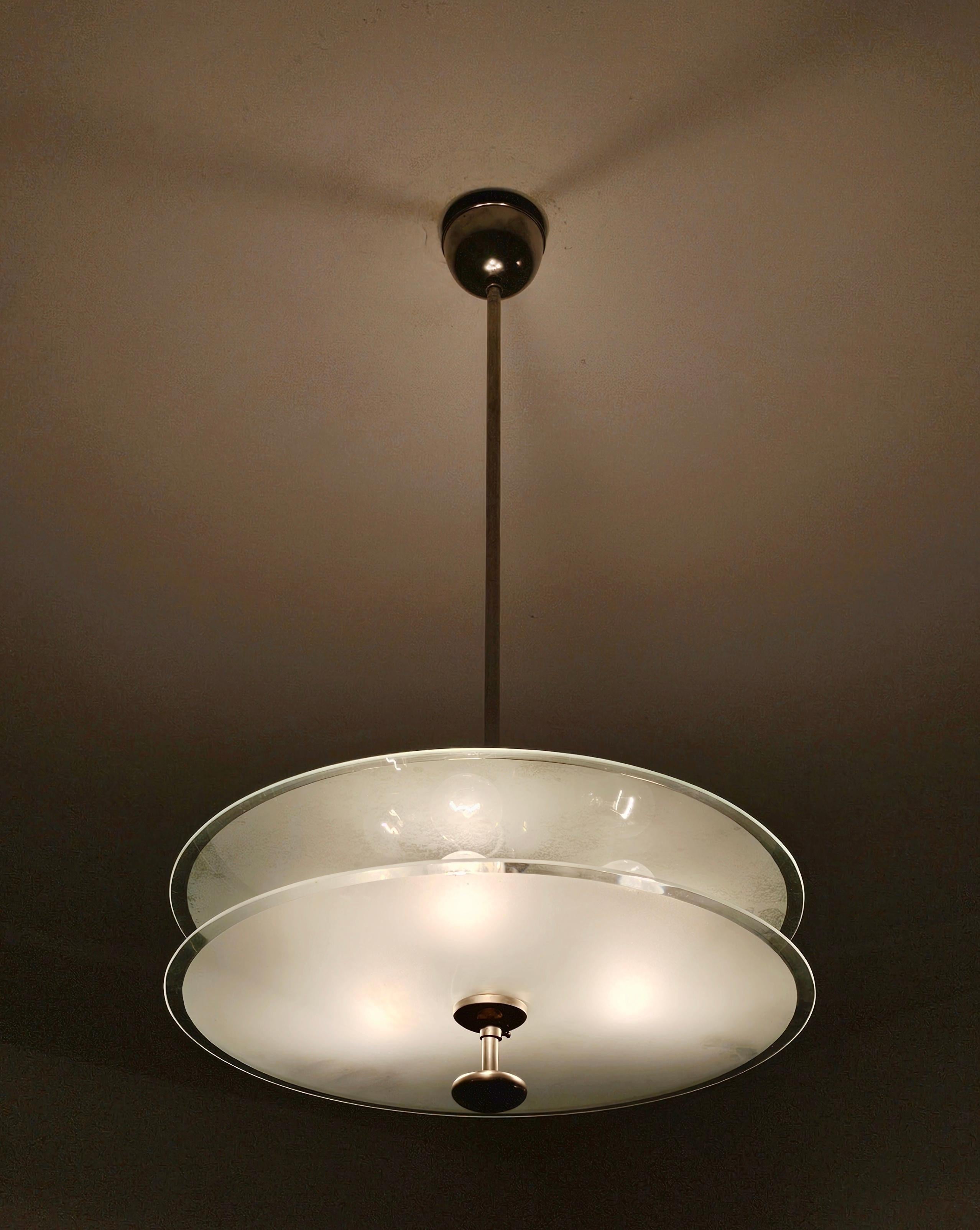 In this listing you will find a very rare, sleek Bauhaus chandelier done in glass and nickel plated brass. It features two glass plates in between which are placed 3 light bulbs, model E27 with European screw. The height of the shade is slightly