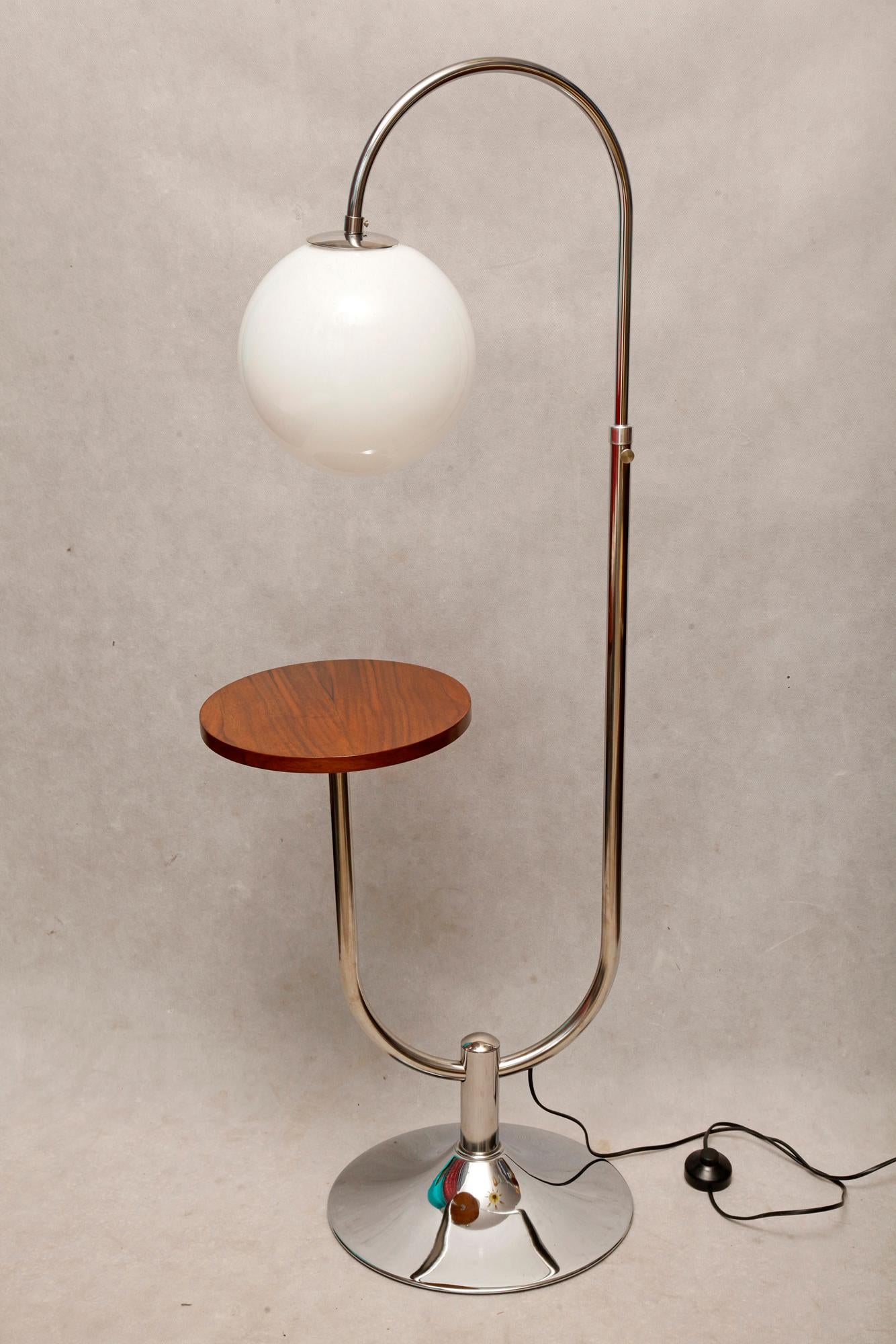 Bauhaus floor lamp was designed by Robert Slezak in the 1930s for the company Slezaky Zavody, known for producing tubular furniture. It features a chrome-plated base, a walnut shelf, and the original glass shade. In 1908, Robert Slezak opened a