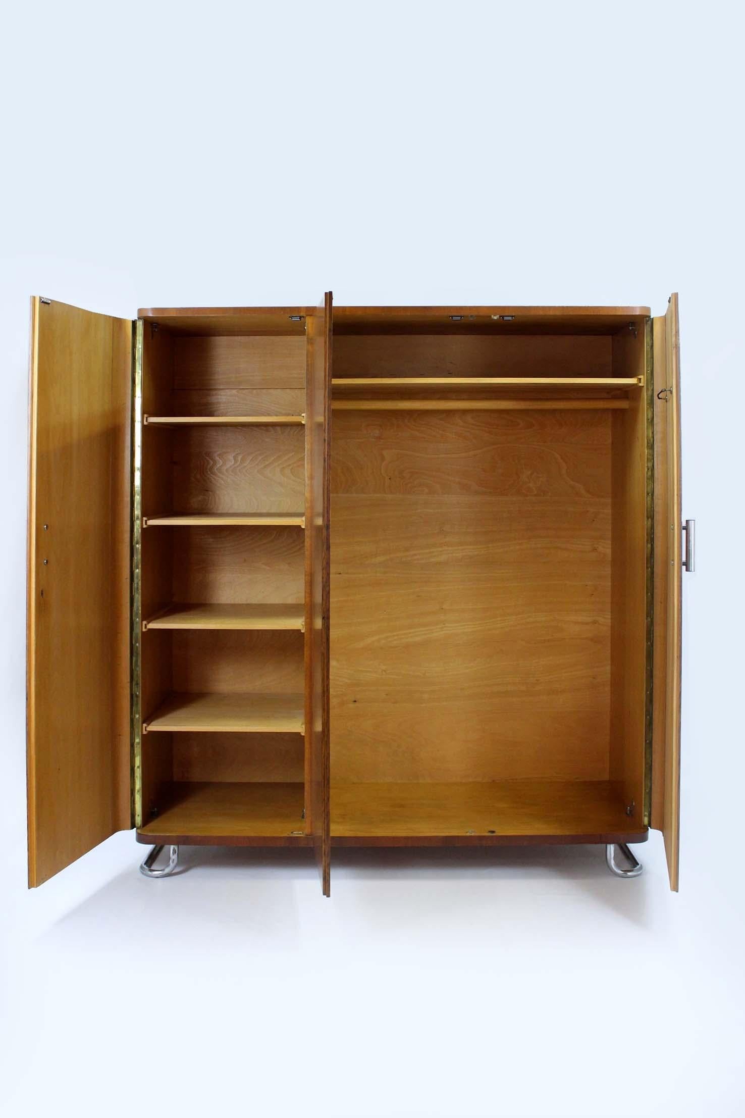 This Bauhaus-style wardrobe was designed by Hynek Gottwald and produced in Czechoslovakia in the 1940s. Features three doors, an internal clothes rail and five shelves. The wardrobe stands on chromed feet and has chromed cylinder handles. The key