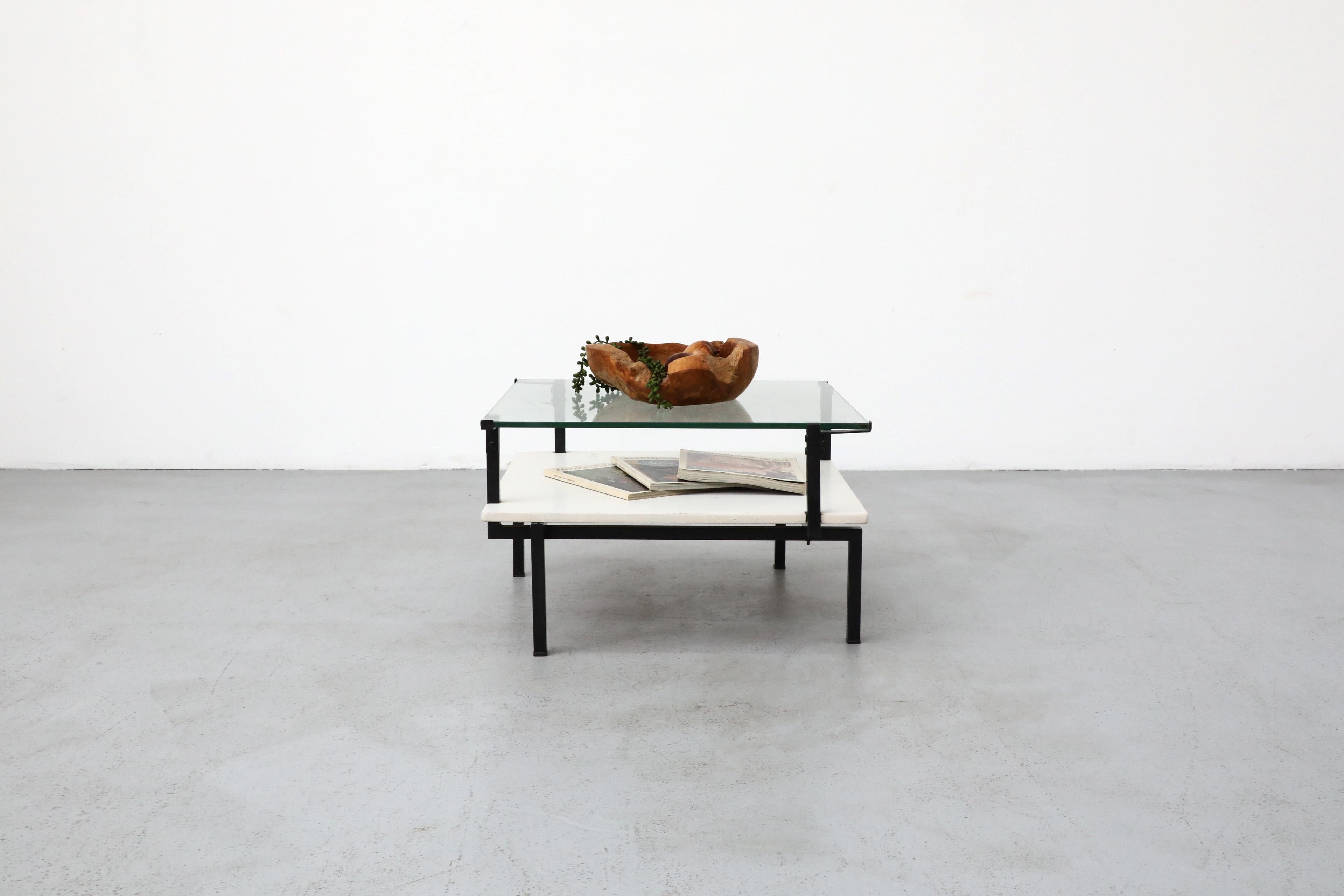 Bauhaus Modernist coffee table with black enameled frame and plate glass top. The table features a unique design with an angular offset enameled metal frame that zags through the lower white wood shelf and providing functional support in its angles