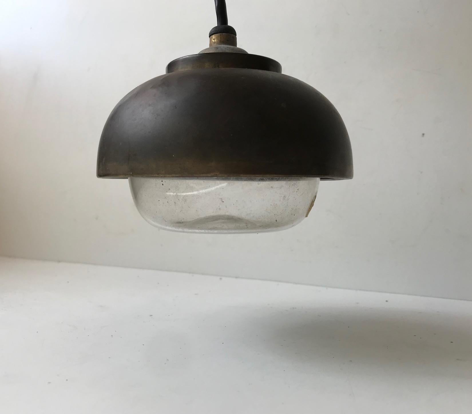 A rare small nautical brass and clear glass pendant light. The shade has patinated extensively of the years. But there are no dents or damages to the shading. It still has its original porcelain and brass socket. It still works and is to be mounted
