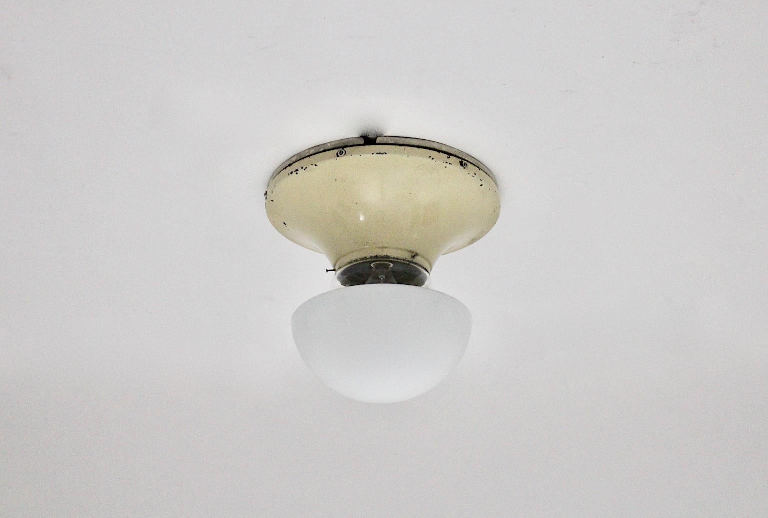 A Bauhaus era white glass metal vintage flush mount, which was designed and produced in the 1930s in Germany.
The flush mount comprises an opaline glass shade fixed on an original white painted metal base. It requires an E 27 light bulb and is in