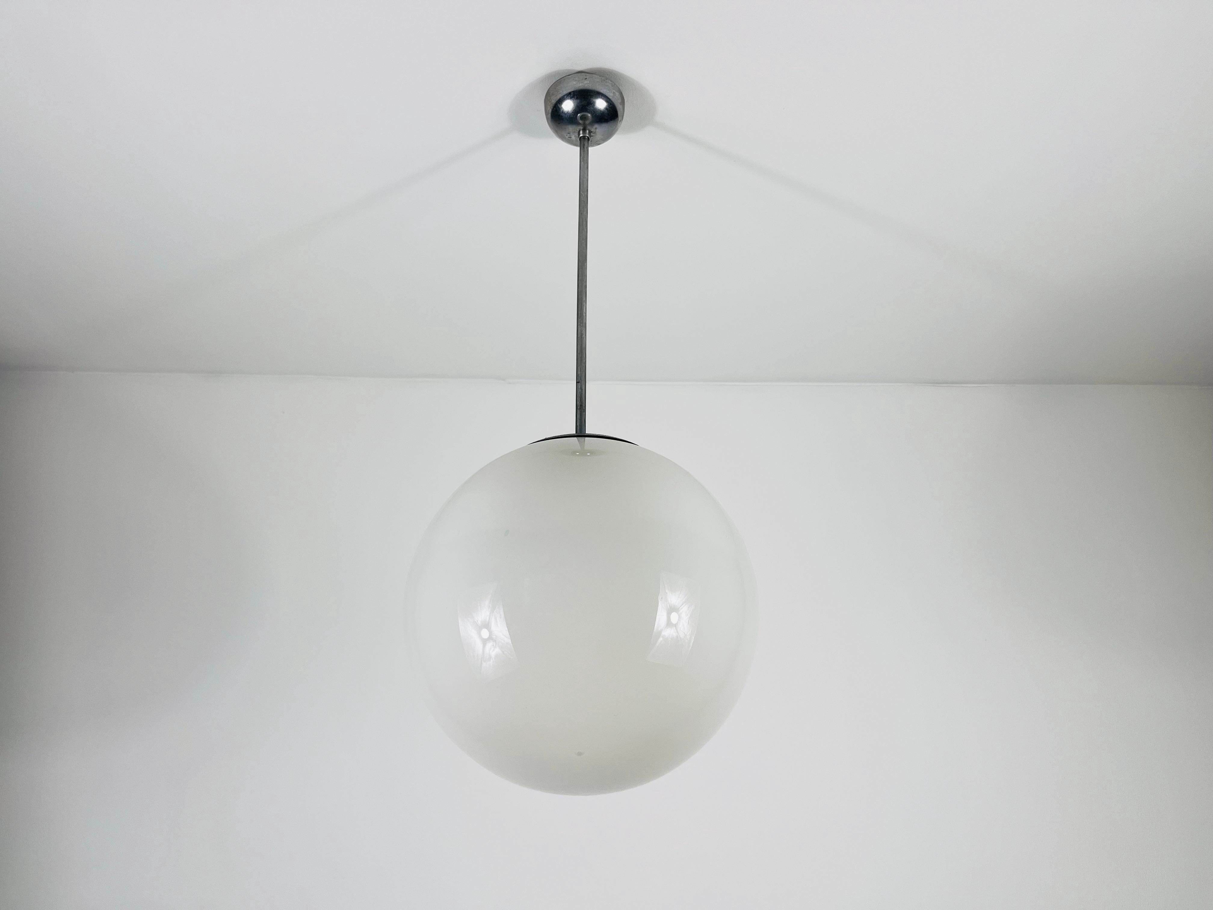 Cette lampe Bauhaus des années 1960 présente un design épuré et minimaliste, fidèle aux principes du mouvement Bauhaus. La lampe est dotée d'un abat-jour en verre opale blanc qui diffuse magnifiquement la lumière, créant une lueur douce et