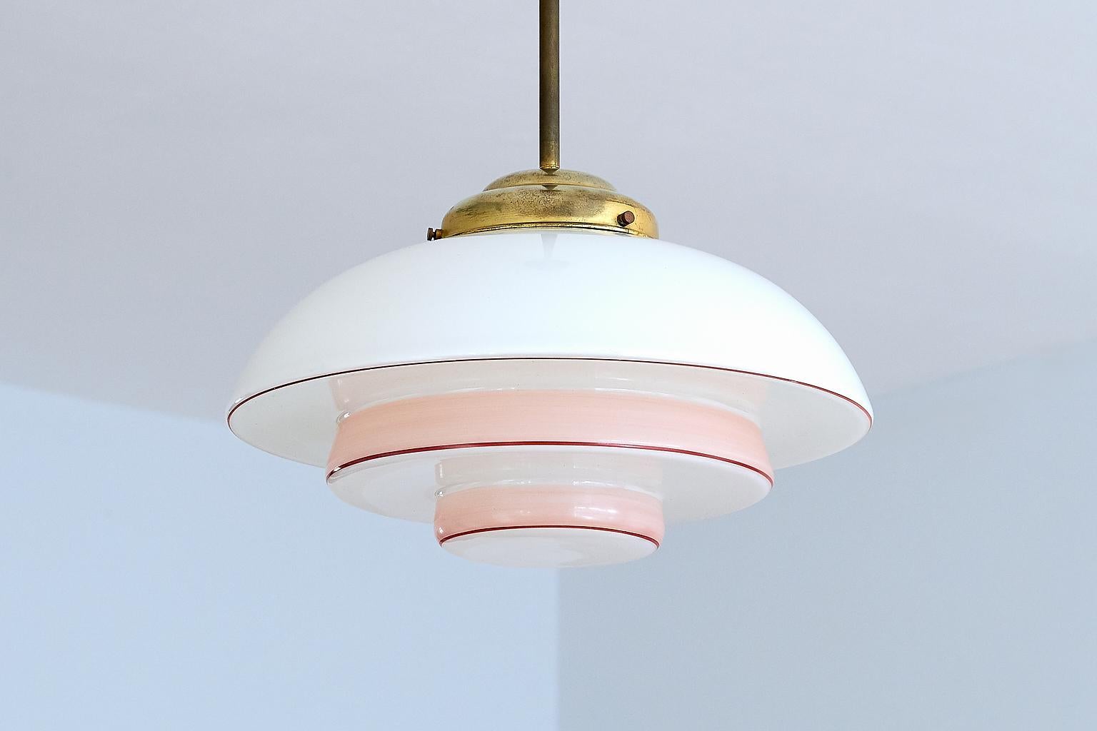 This three-tier Bauhaus pendant or ceiling lamp was produced in Germany in the early 1930s. The different layers of the opaline glass shade are emphasized by the use of color. The two pink colored tiers and the painted red circular line accentuate