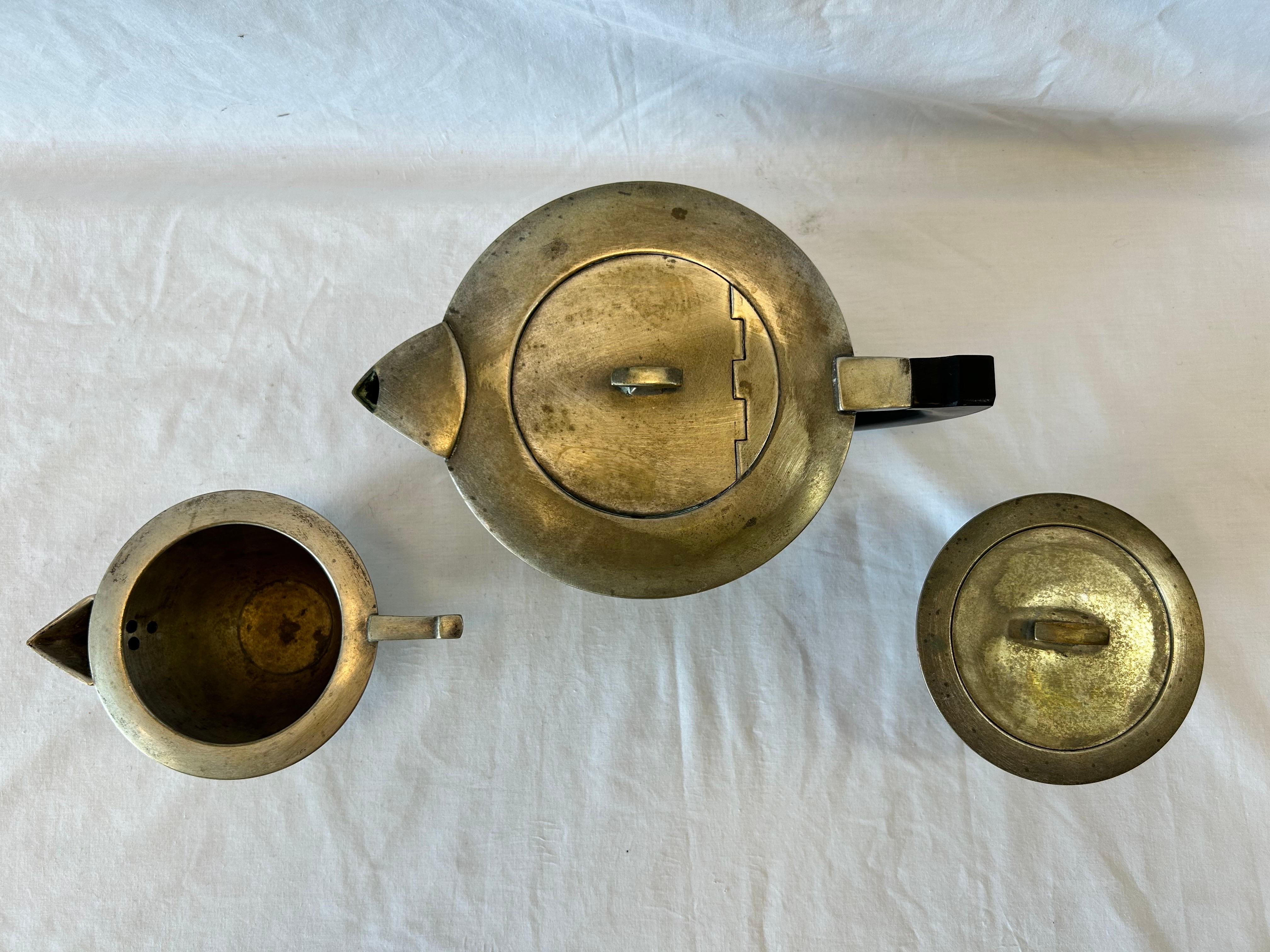 A three piece silver plate tea set of Bauhaus sensibility in the style of Marianne Brandt. The service consists of a teapot, a creamer and a covered sugar. All pieces are unmarked. I believe the handle of the teapot is composed of Bakelite. The