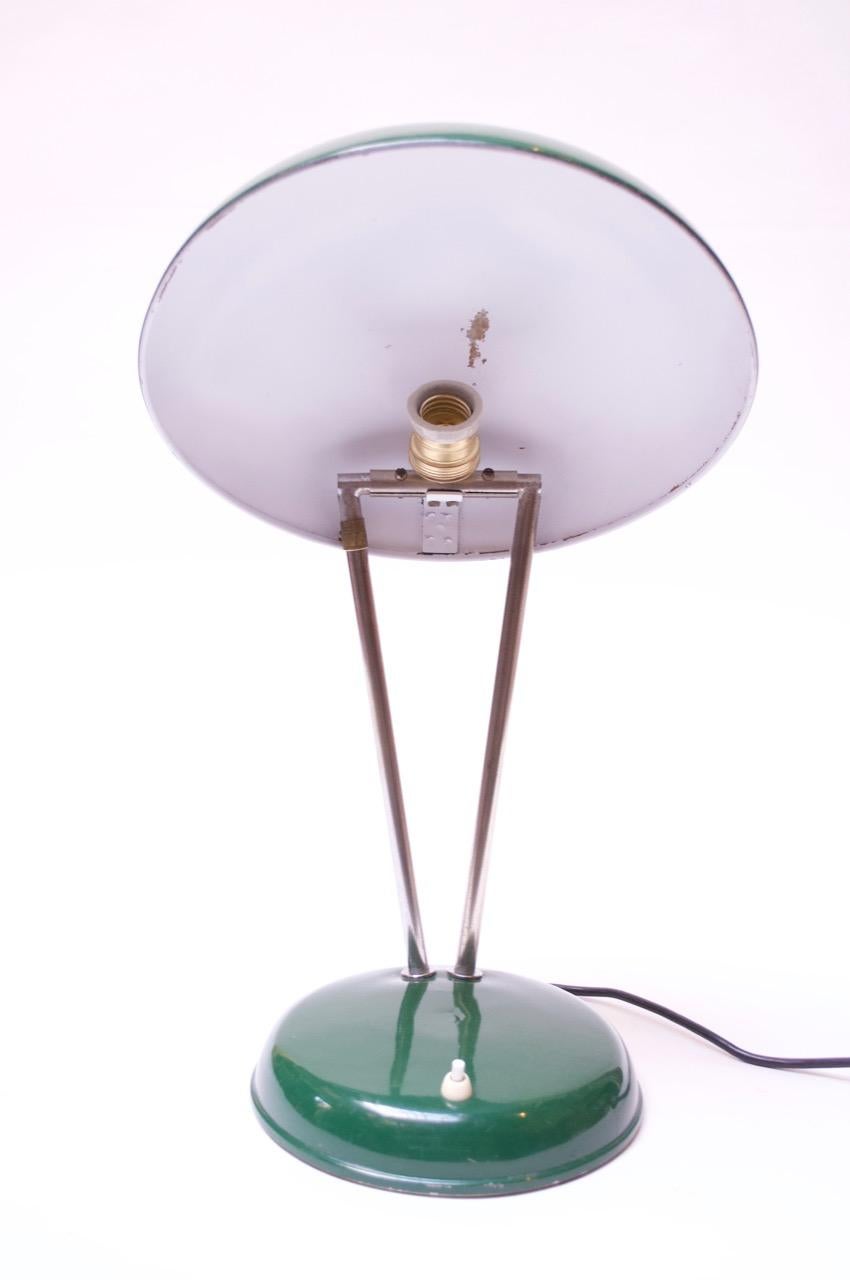 Table lamp composed of an adjustable enameled-metal shade and base with a dual chromed-metal stem, circa late 1940s-early 1950s. Retains the original green enamel paint. Brass medallion engraved 'P 116' affixed to one of the stems.
Light scuffs /