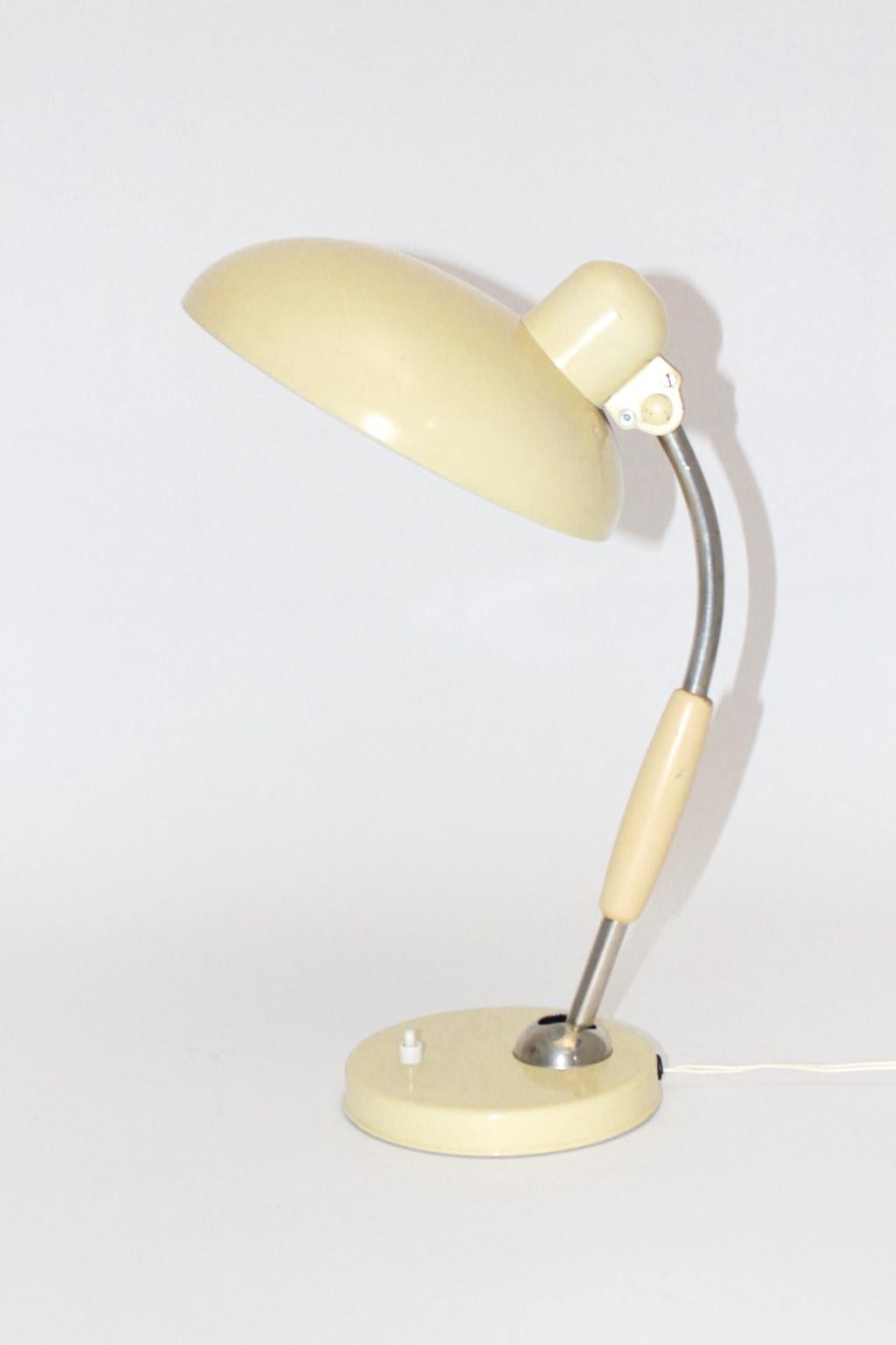 This ivory colored table lamp was designed by Christian Dell 1933 and produced by Koranda, Germany, circa 1950. Furthermore the table lamp was made of metal and wooden parts. Also the table lamp features joints, which allow to swivel and to