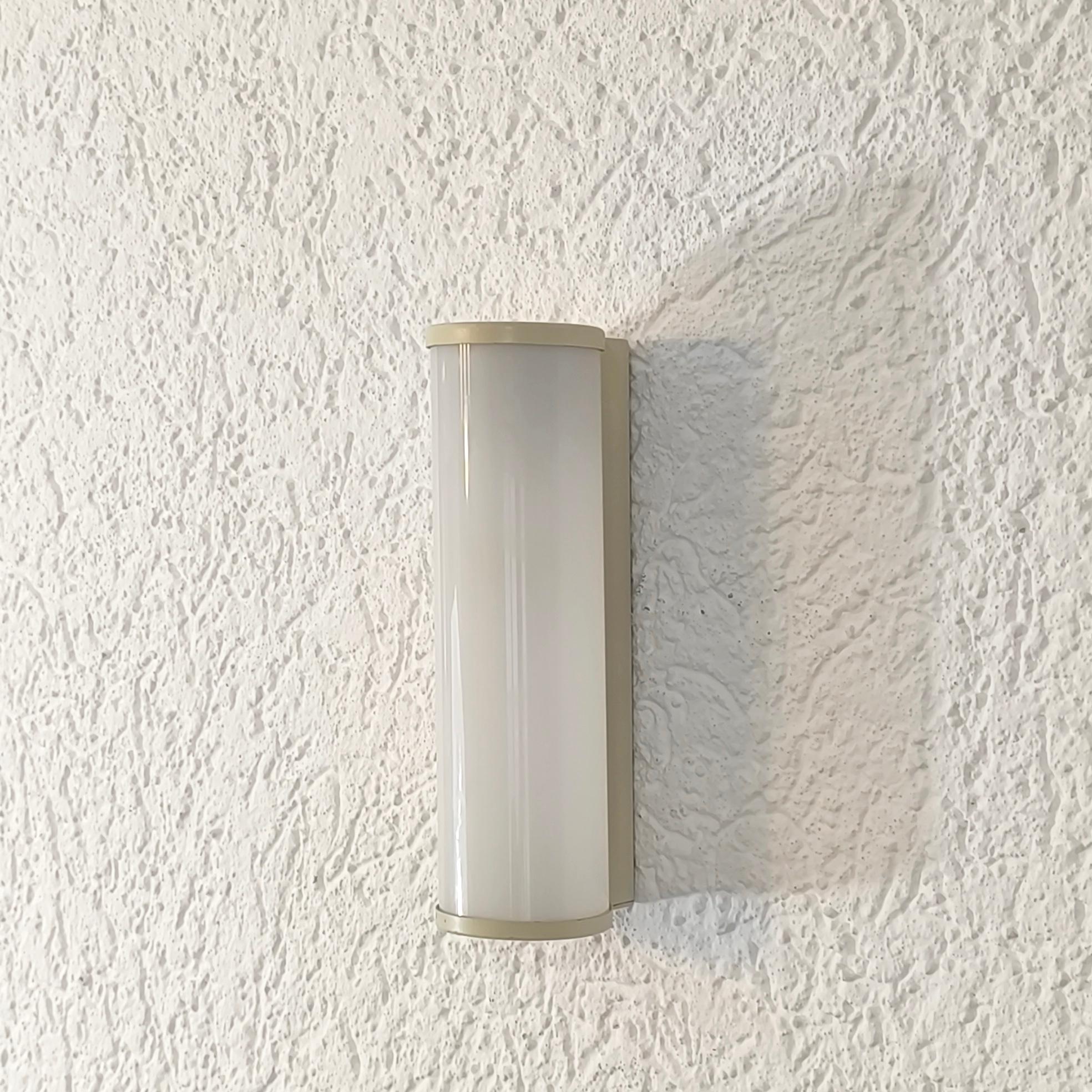 Cylindrical sconce with cased glass shade from the 1930s-40s, in Bauhaus / Art Deco style.

This is a simple and elegant piece with metal wall plates and end caps. It houses a milky cased-glass shade.

The light is in good condition, with a warm