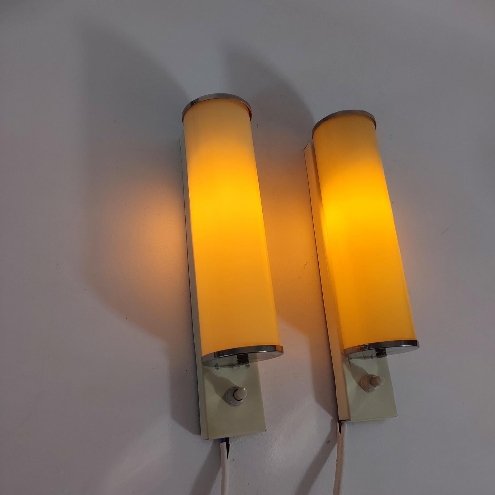 Pair of cylindrical sconces with cased glass shades, and switch-on to the bottom, from the 1930s-40s, in Bauhaus / Art Deco style.

Simple and elegant pieces with metal wall plates and end caps, which house cased-glass shades with an outer layer of
