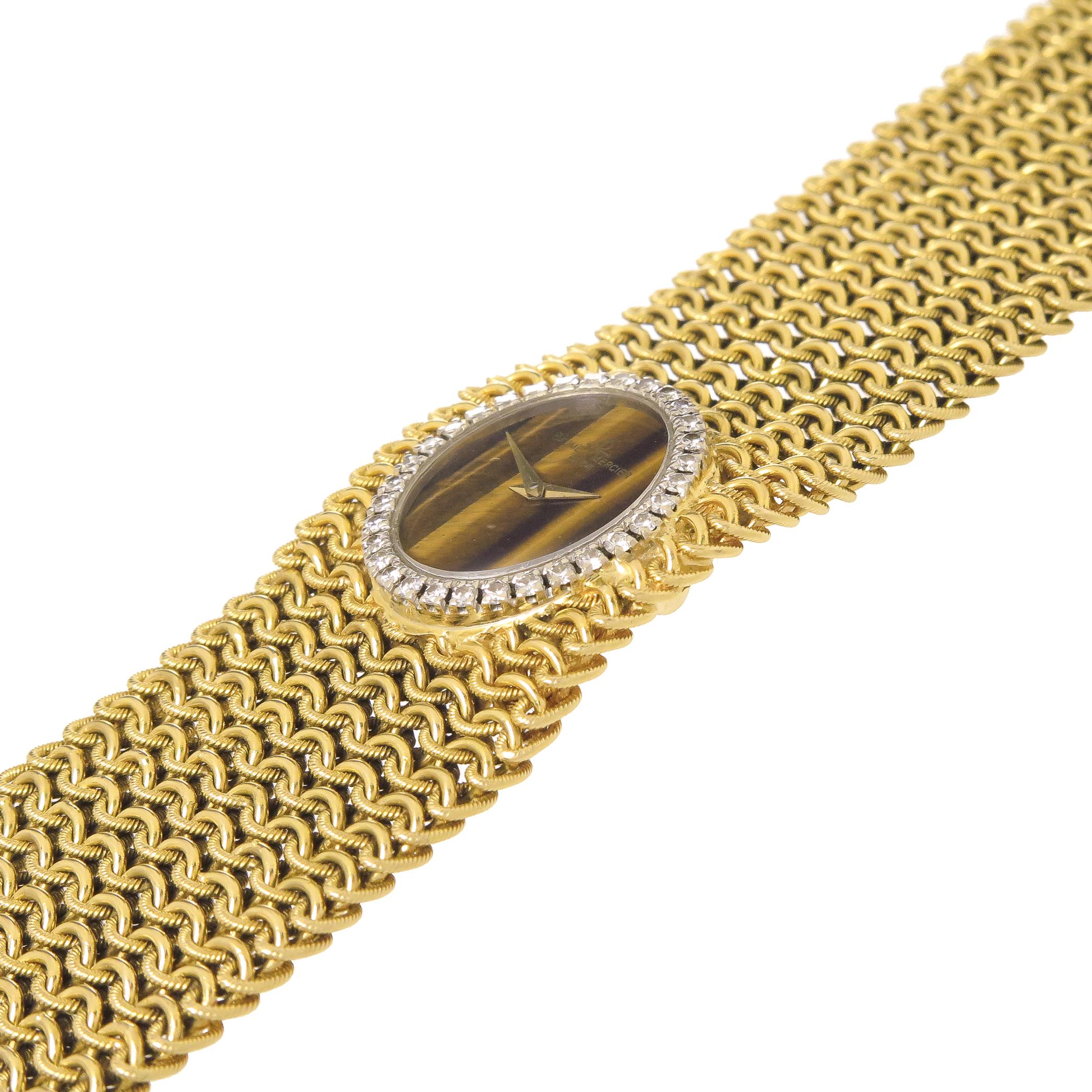 Circa 1970s Baum & Mercier Ladies 18K Yellow Gold Bracelet Wrist watch, a soft and flexible mesh link bracelet measuring 7 inches in length and 1 3/16 inch wide. White Gold Bezel set with Round Brilliant cut Diamonds totaling 1 Carat. Tigers Eye