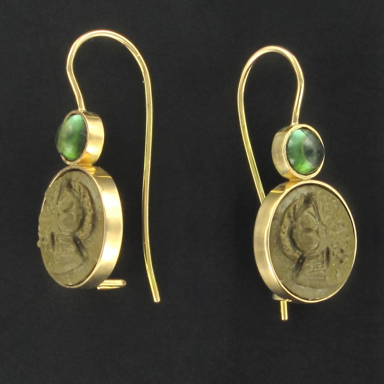 Creation Baume - Unique piece.
Earrings in 18 carats yellow gold.
Lovely drop earrings, each are set closed with a cameo on lava stone representing a helmeted warrior and surmounted by a tourmaline cabochon also set closed. The clasp is a gooseneck