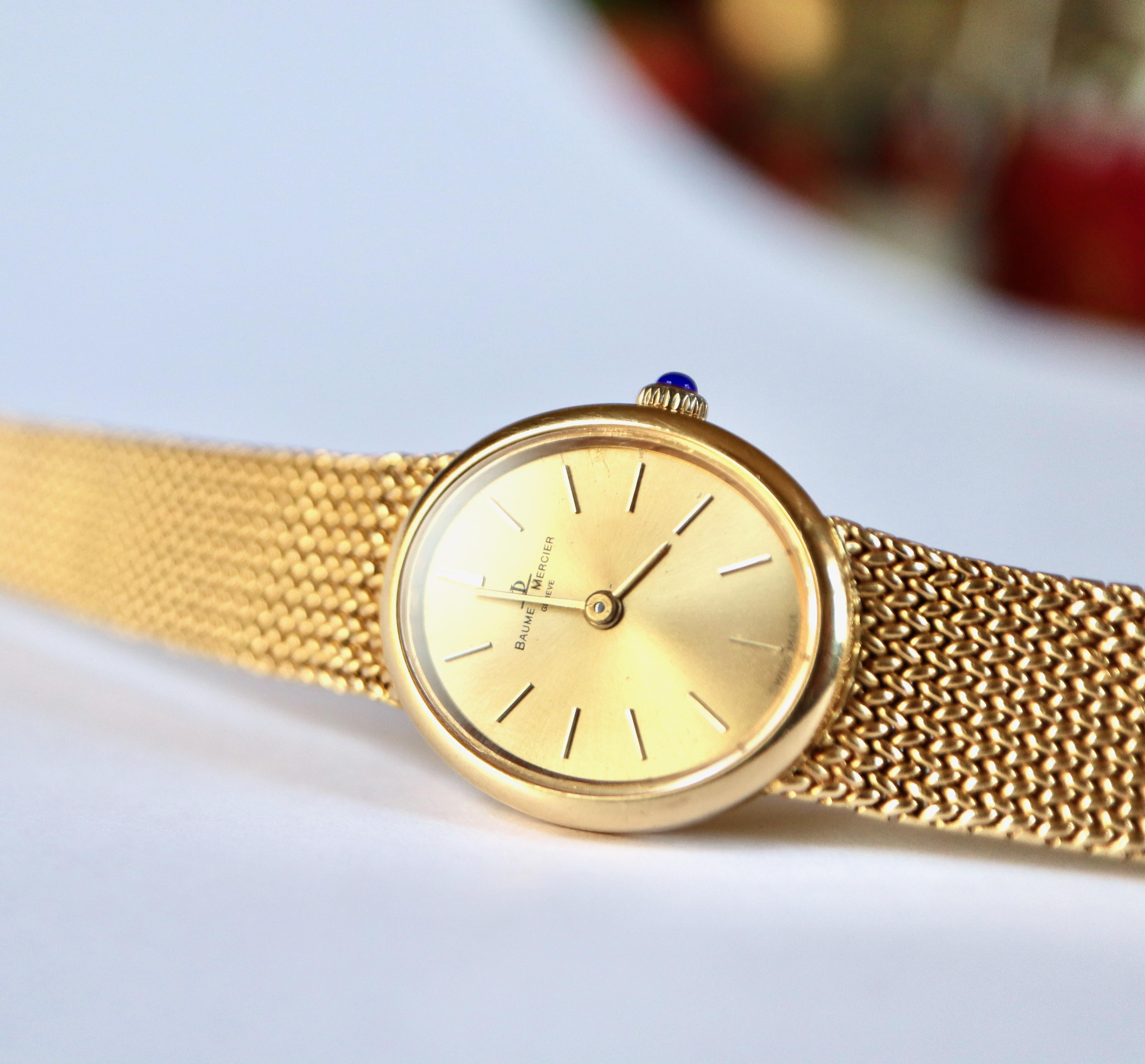 Baume et Mercier lady's wristwatch in 18 kt yellow gold, oval dial mechanical movement. Golden background, applied baton indexes. Winder set with a sapphire cabochon. Flexible bracelet, braided link with adjustable position ratchet clasp, circa