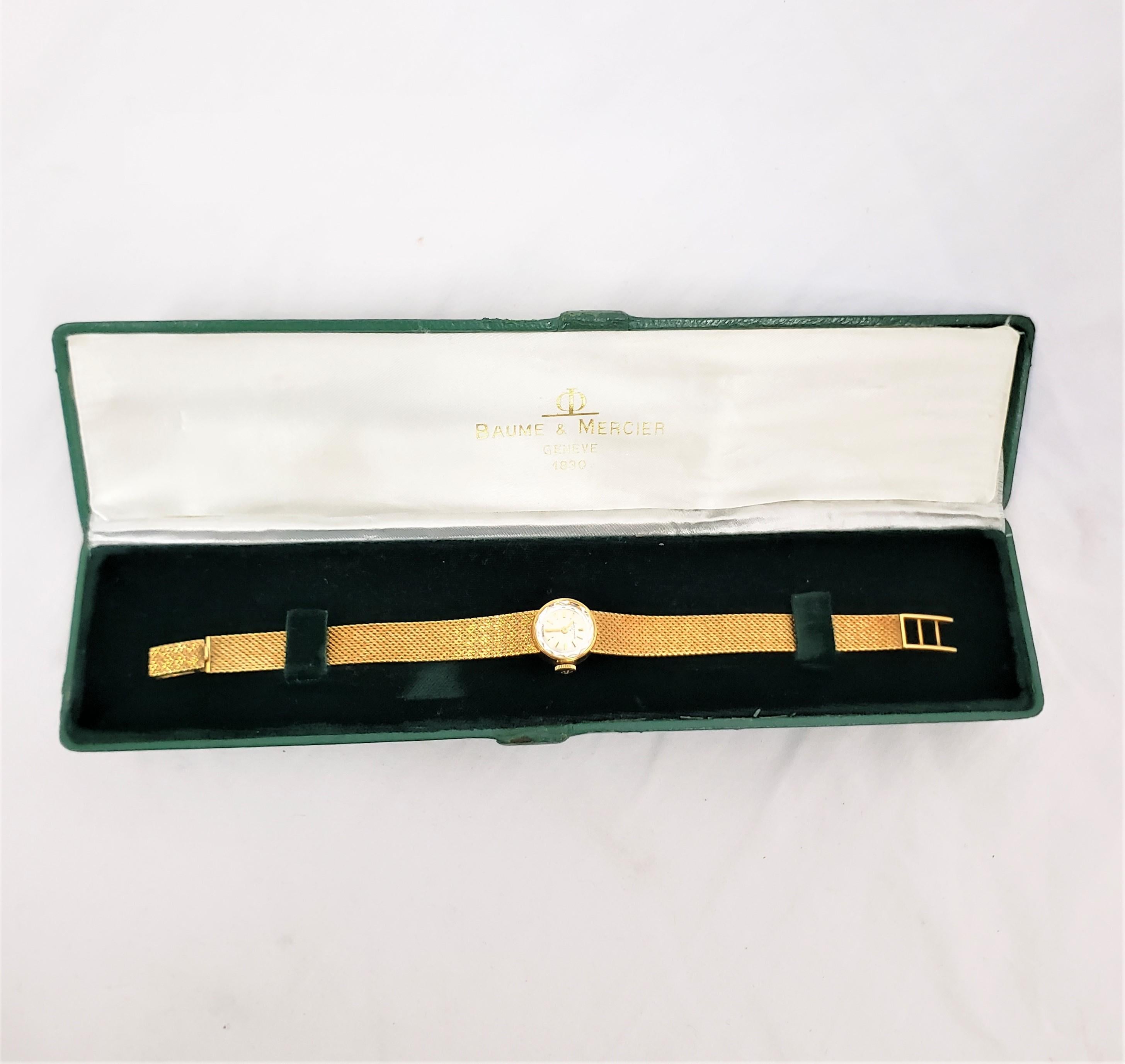 Diese antike Damenarmbanduhr wurde von der bekannten Firma Baume et Mercier aus der Schweiz um 1920 im Stil der Zeit hergestellt. Die Uhr und das Armband bestehen aus achtzehnkarätigem Gelbgold. Das Zifferblatt ist in einem silbernen Ton mit einer