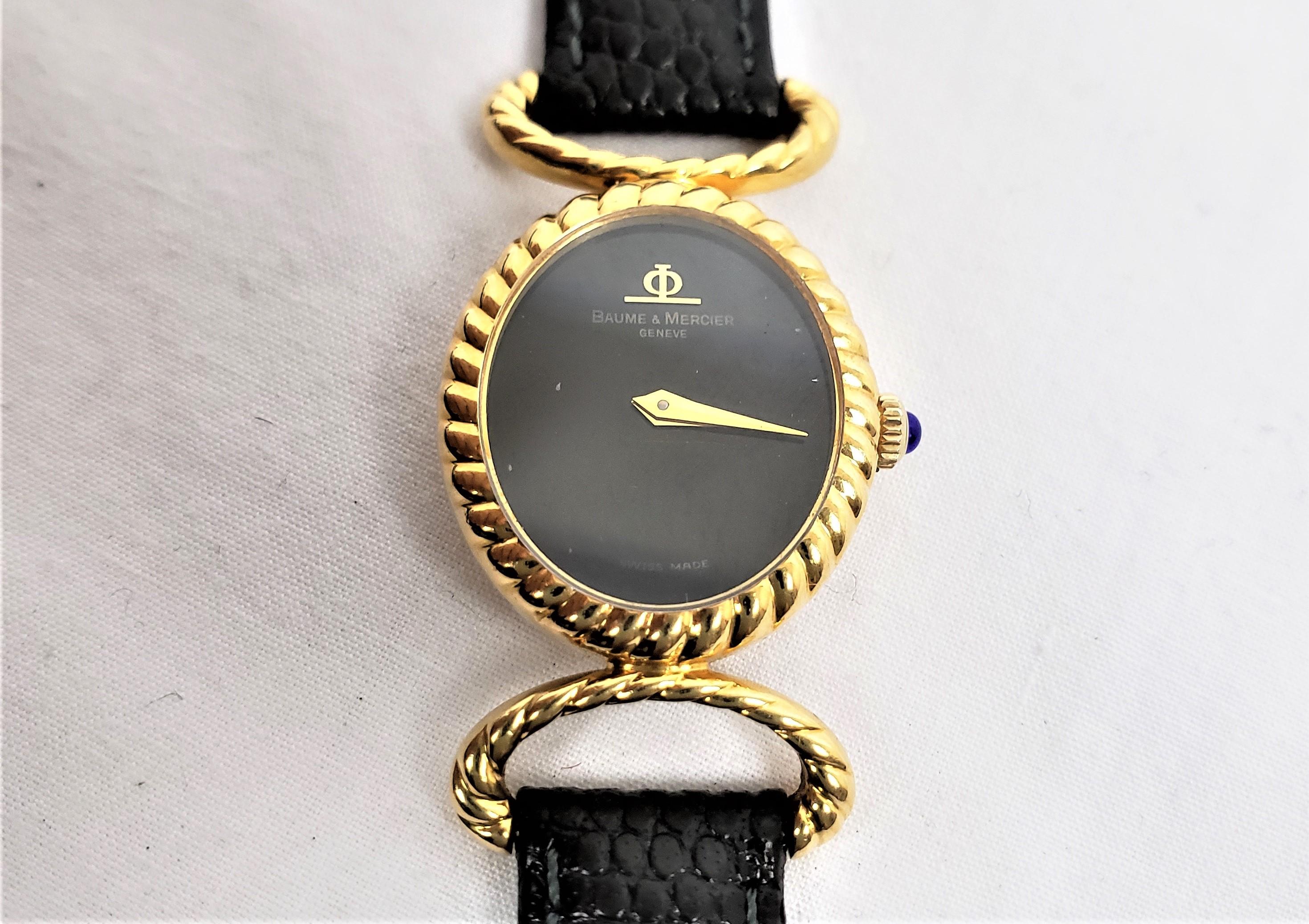 Diese Damenarmbanduhr wurde von der bekannten Baume et Mercier aus der Schweiz um 1970 im Stil der Jahrhundertmitte hergestellt. Die Uhr und die Bandanstöße sind aus achtzehn Karat Gelbgold gefertigt. Das Zifferblatt ist schwarz und mit goldenen