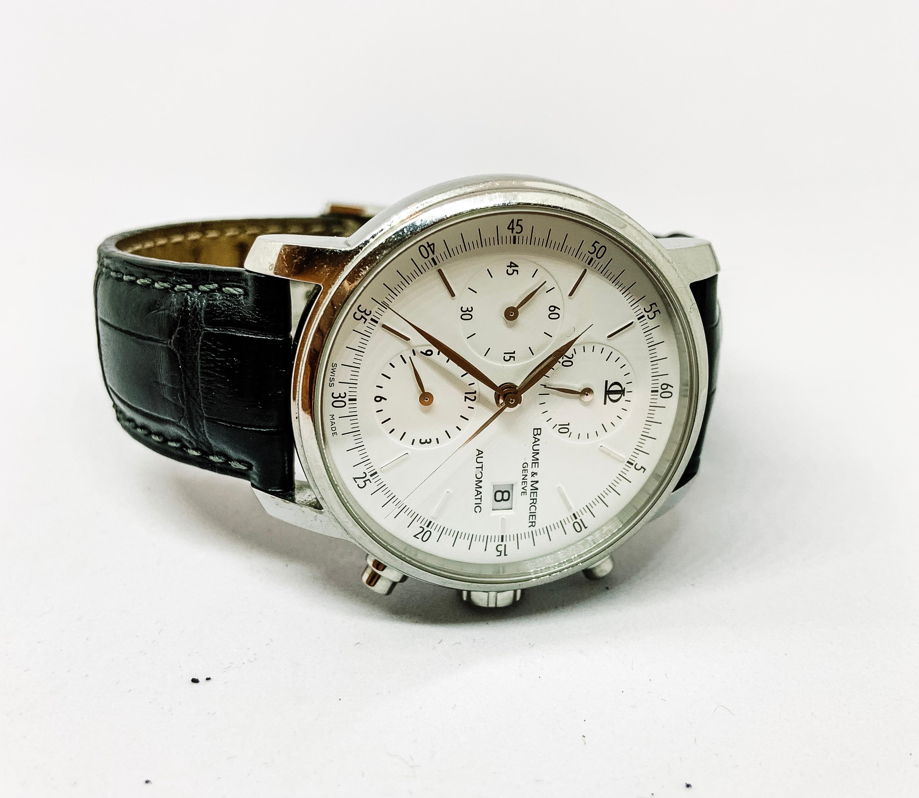 One Stainless Steel Automatic Watch Made In Geneva And Designed By Baume & Mercier Gentlemen's Wrist Watch with black crocodile leather band and an all white face with date window and chronograph on the face of the watch. 
Manual, Limited Warranty