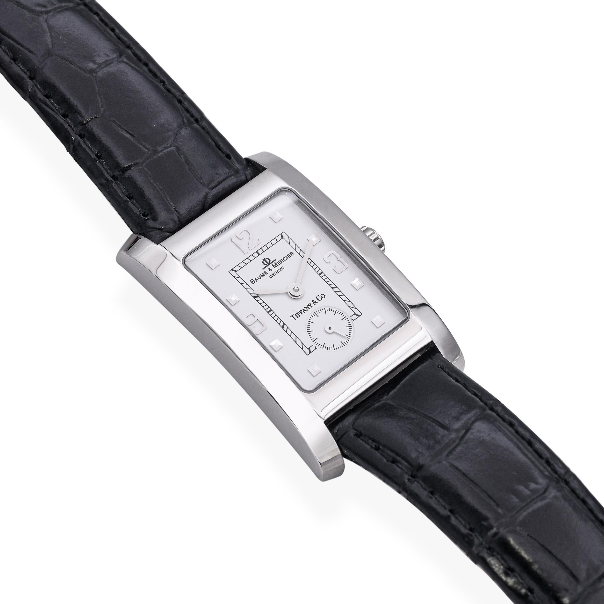 This Baume & Mercier x Tiffany & Co. men’s tank-style watch features a sleek stainless steel case with sharp Art Deco lines and refined proportions. The minimalist silver dial is elegantly marked with Roman numerals and slim black hands, capturing a