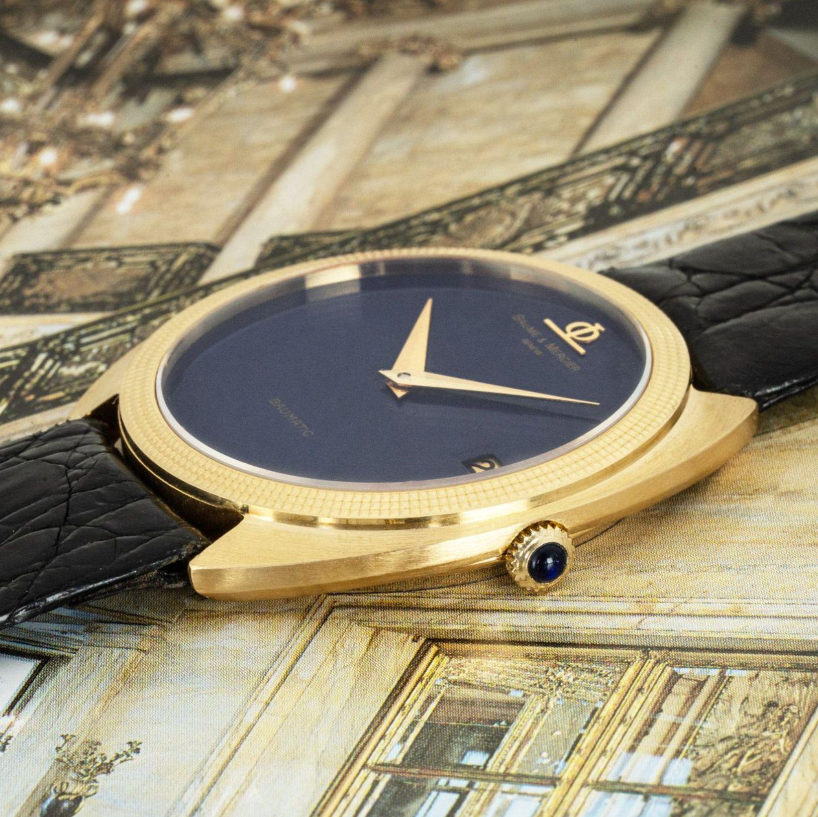 A 36mm yellow gold mens Baume & Mercier wristwatch. Featuring a stunning a lapis dial, a date aperture and a yellow gold bezel. The watch is fitted with a sapphire glass, a self-winding automatic movement and a Baume & Mercier black leather strap