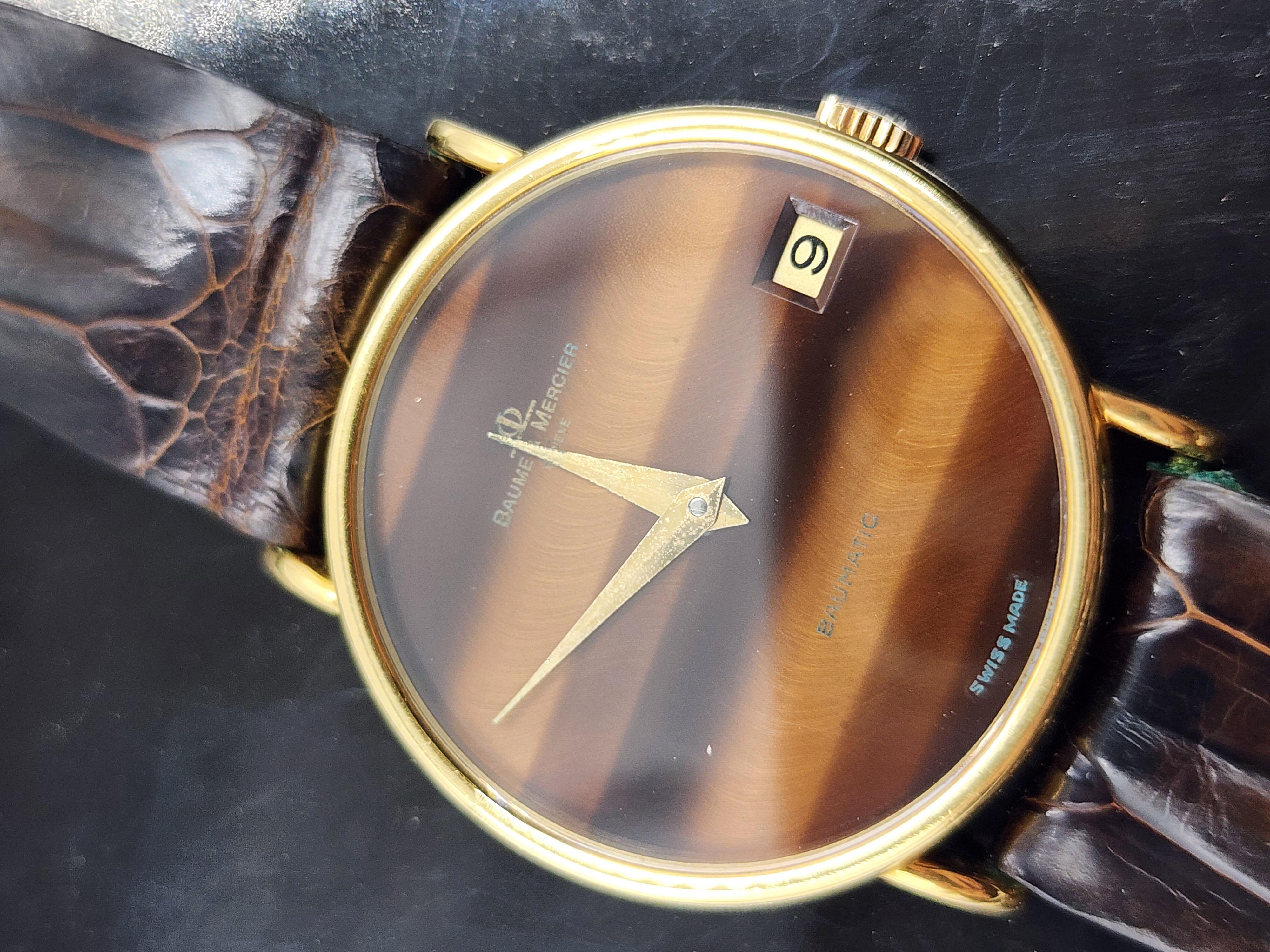 Baume & Mercier 18 kt Gold Vintage Men's Calendar Watch
Beautiful Baume & Mercier 18 kt gold watch with tiger's eye dial and integrated calendar, leather strap with branding on the inside, which has wear and tear from use.
Although the watch is for