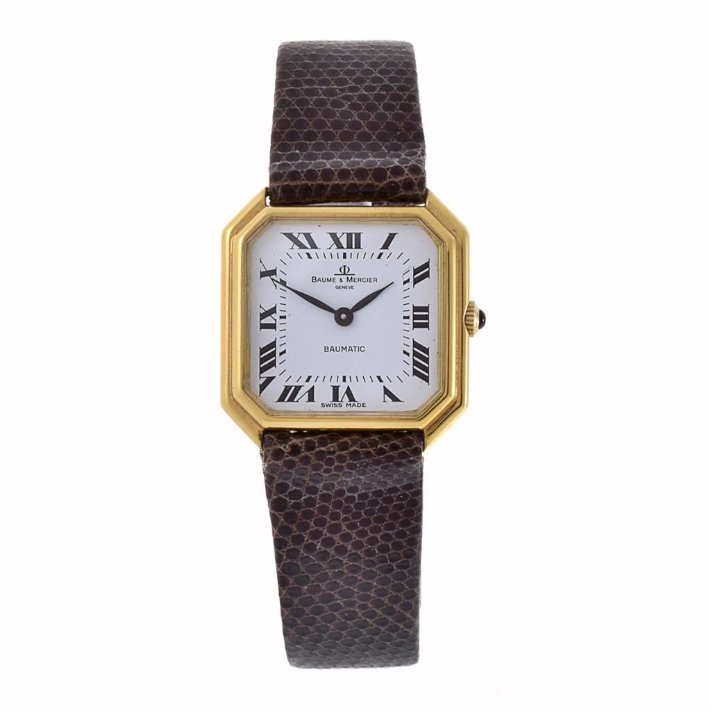Diese Baume & Mercier Uhr ist Vintage; sie stammt aus den 1970er Jahren. Sie hat ein weißes Zifferblatt, ein 27 mm x 27 mm großes Gehäuse aus 18-karätigem Gold und ein schwarzes Lederarmband. Die Uhr verfügt über ein 30-steiniges Automatikwerk und
