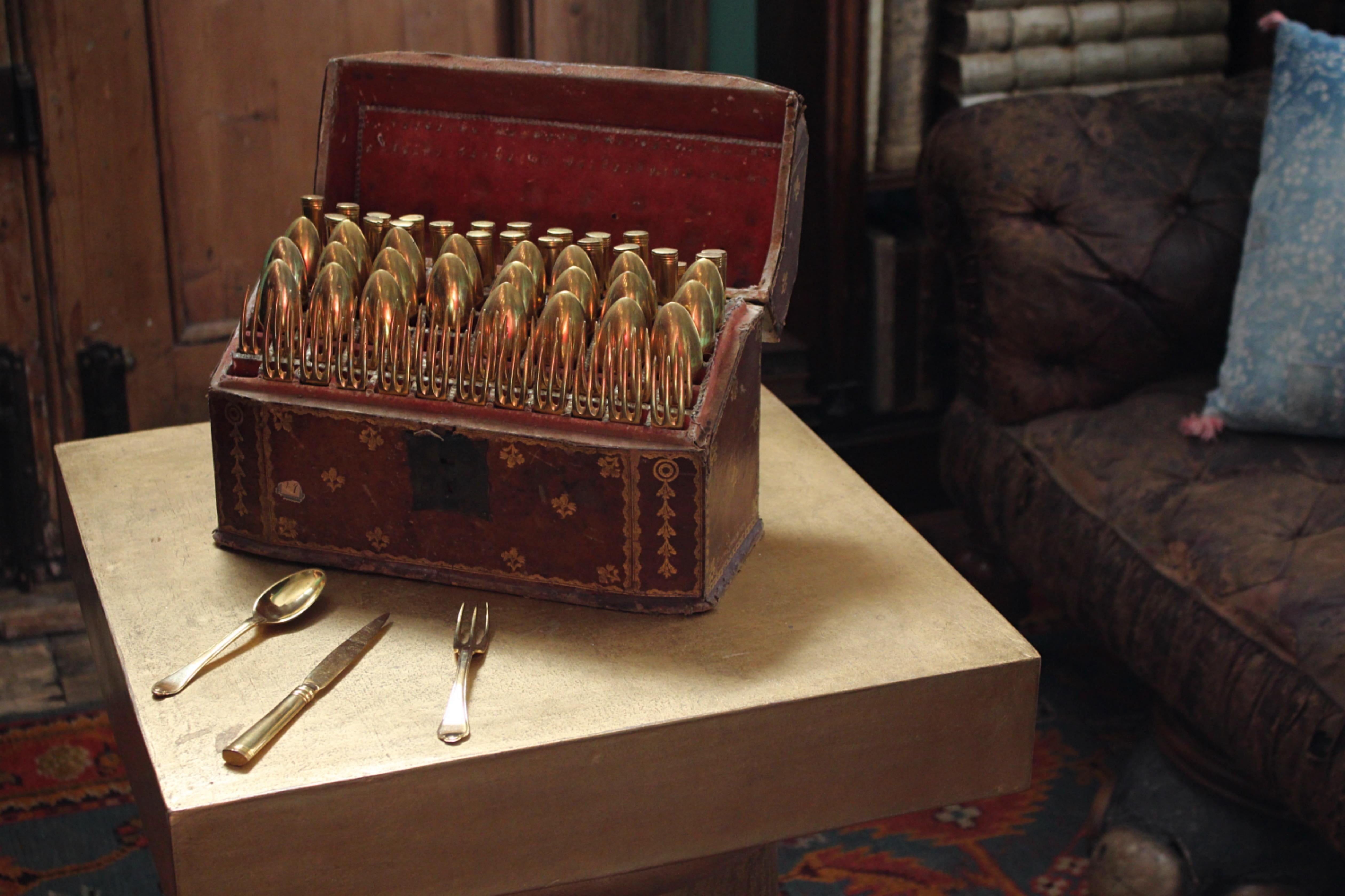A 19th century canteen of gilt copper flatware, in a fitted gilt-tooled leather casket decorated with an armorial and floral sprays.

comprising of twenty-four dessert forks, twenty-four dessert spoons and twenty-three dessert knives (one