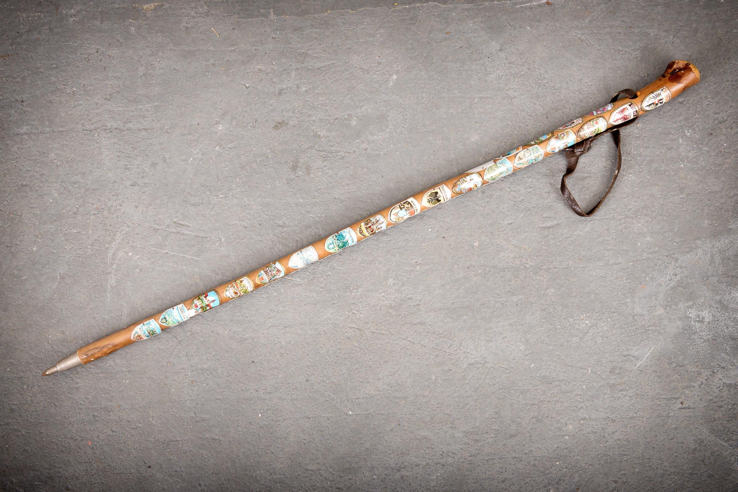 This is a striking example of a European Volksmarch walking stick cane, adorned with a number of colorful badges from various destinations.This walking stick has trekked throughout many wonderful places collecting badges along the way. The cane