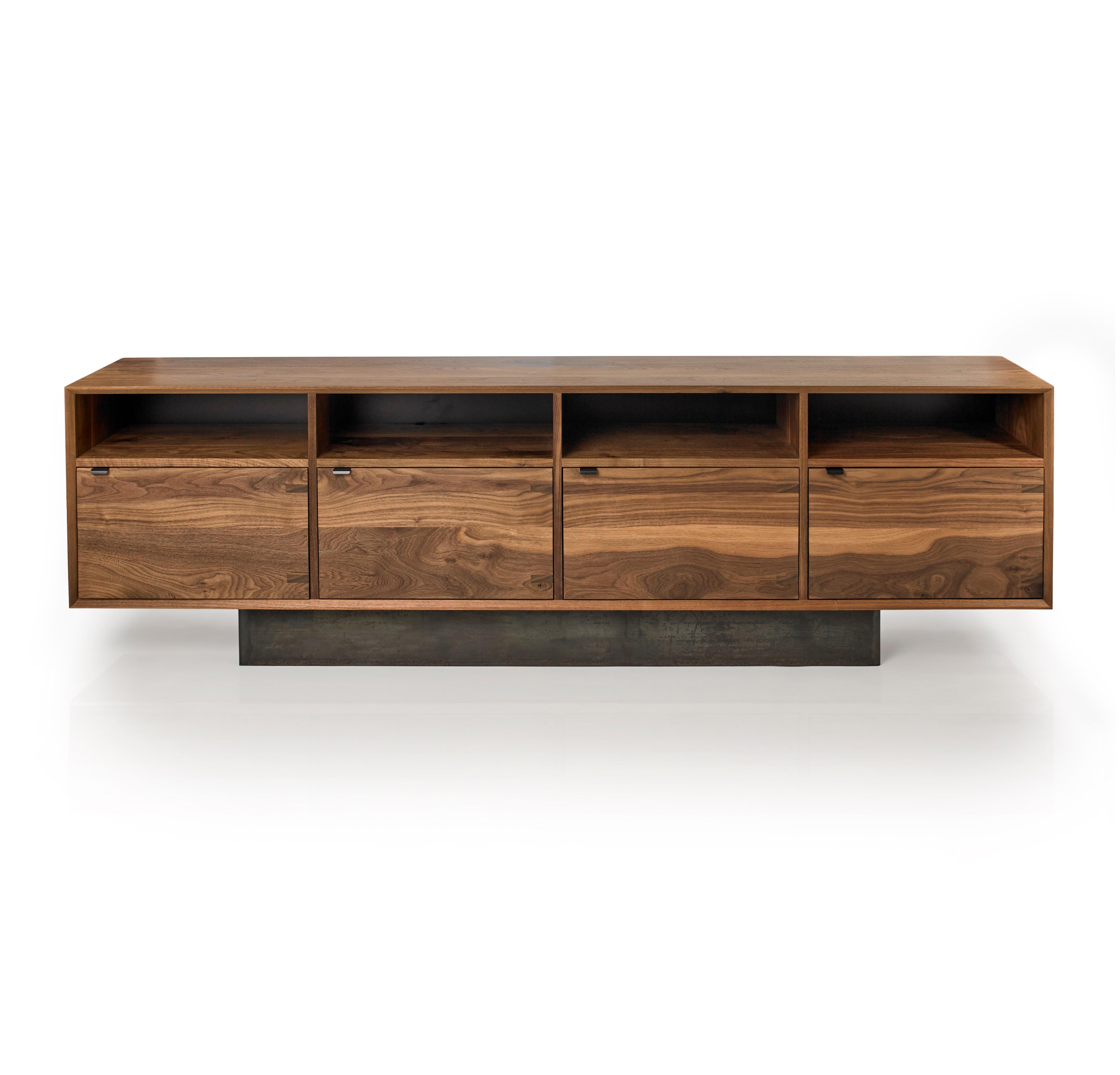 The Baxter Credenza has a low and lean profile, showcasing four cabinet doors and open upper storage. The credenza uses solid black walnut constructed with, an uncommonly practiced, entirely solid wood carcass, cabinet doors, and interior shelves.
