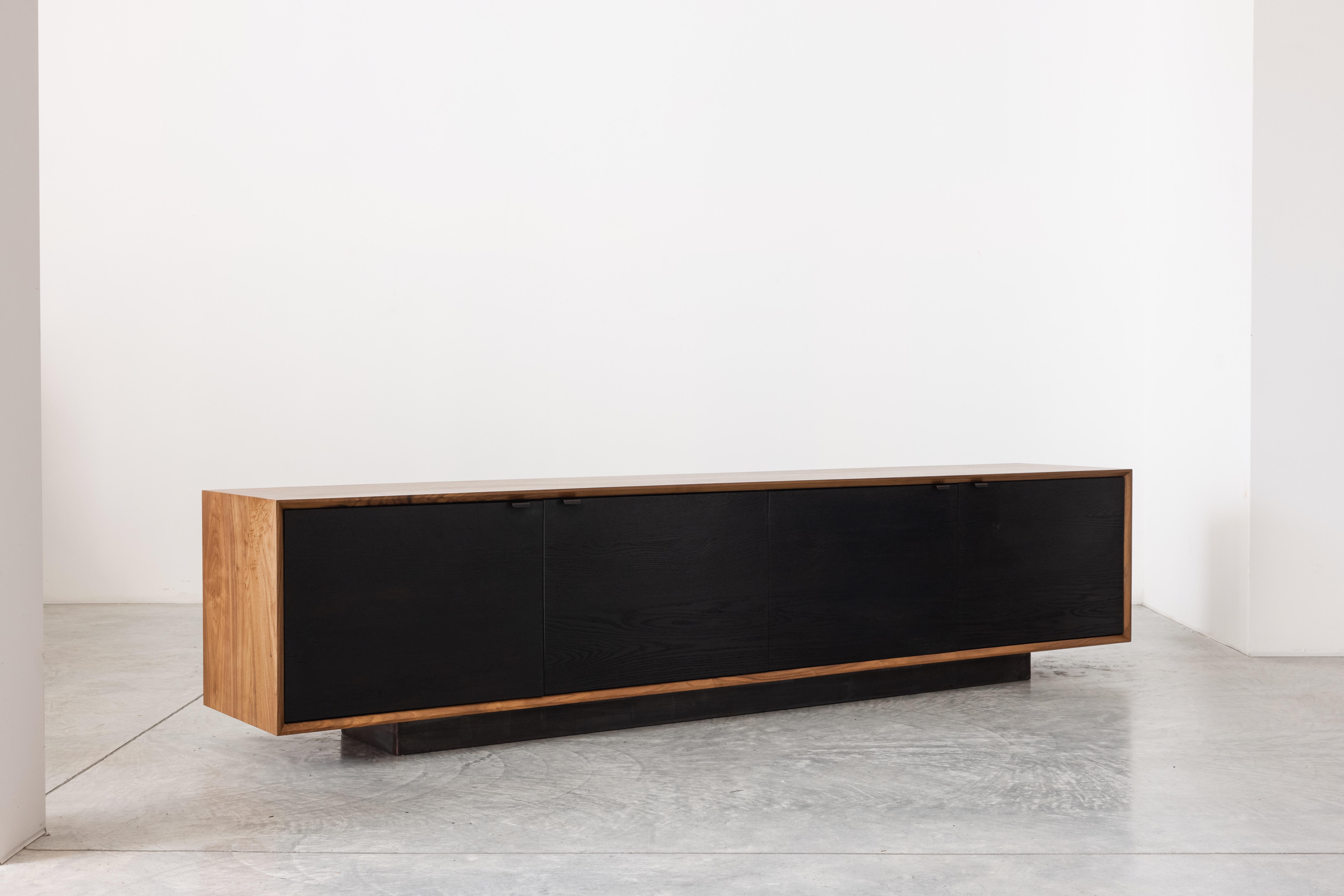The Baxter Low Credenza has a sleek profile, showcasing four cabinet doors. The credenza uses solid black walnut constructed with, an uncommonly practiced, entirely solid wood carcass, and interior shelves. For dramatic contrast, the credenza doors