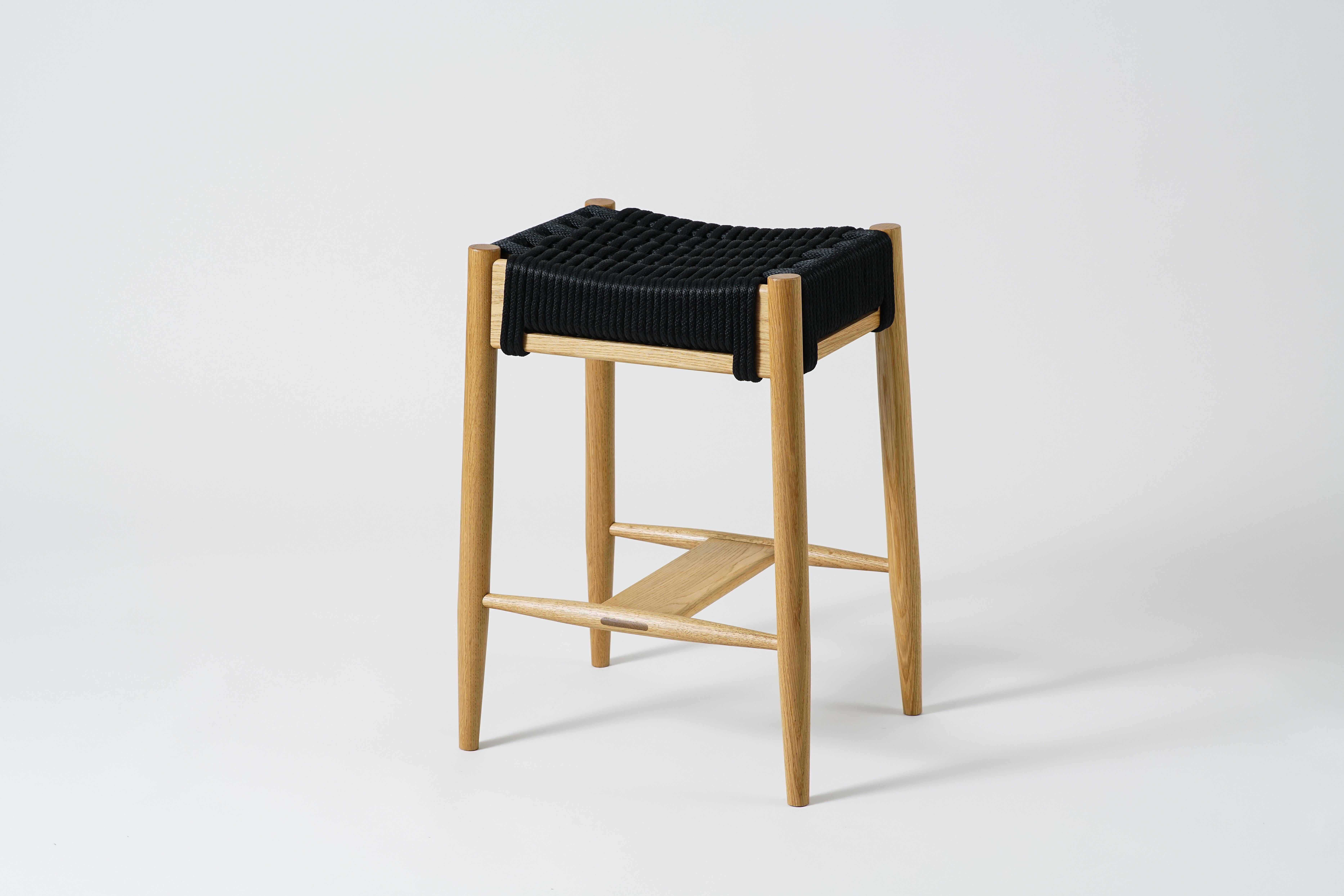 The Bay Counter Stool is a solid wood stool with a roomy seat and turned tapered legs. Wood frames available in walnut, white oak, maple, and black. Available with a rope woven seat (shown here). The sturdy, but graceful footrest has an exposed