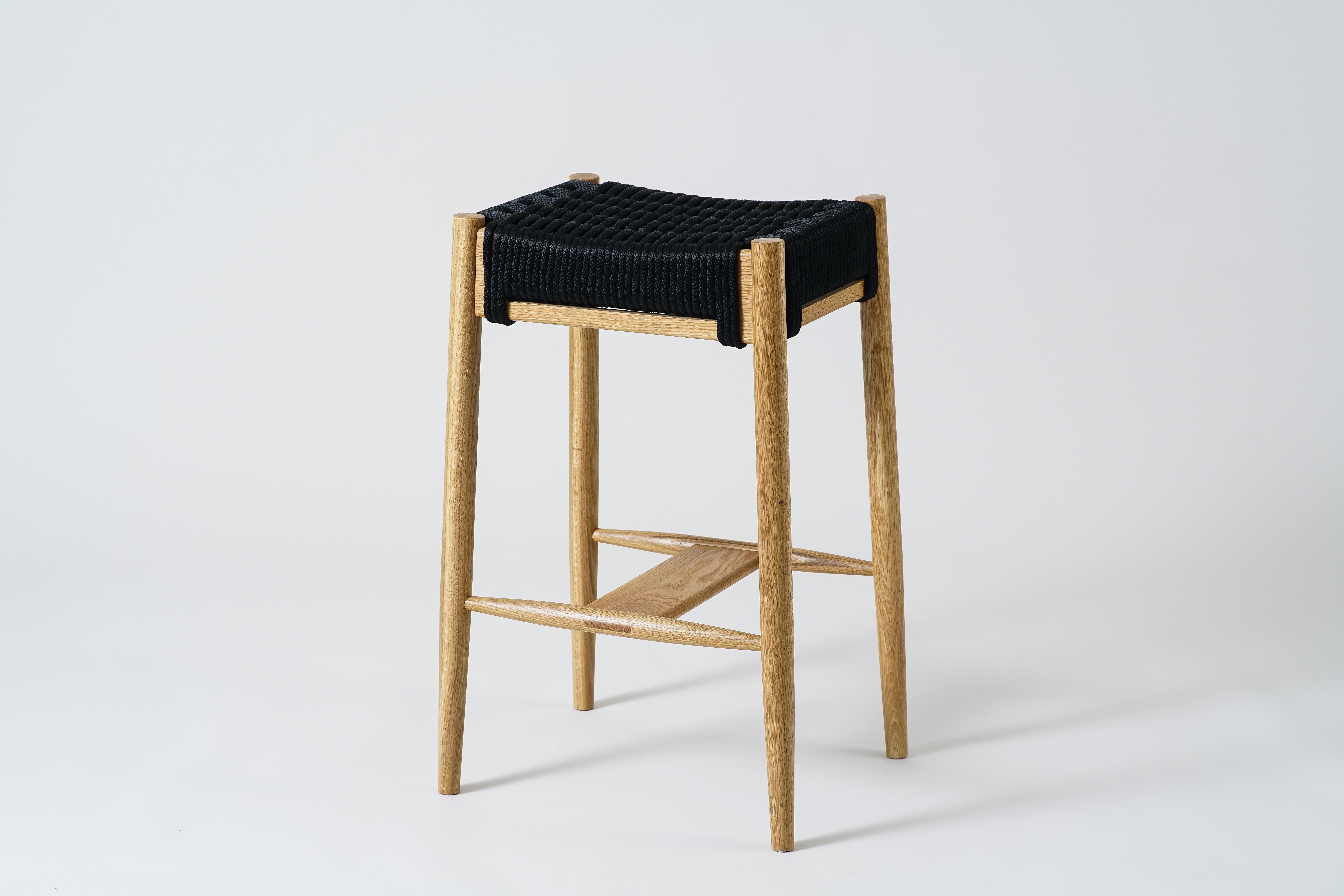 The Bay Bar Stool is a solid wood stool with a roomy seat and turned tapered legs. Wood frames available in walnut, white oak, maple, and black. Available with a rope woven seat (shown here). The sturdy, but graceful footrest has an exposed tenon