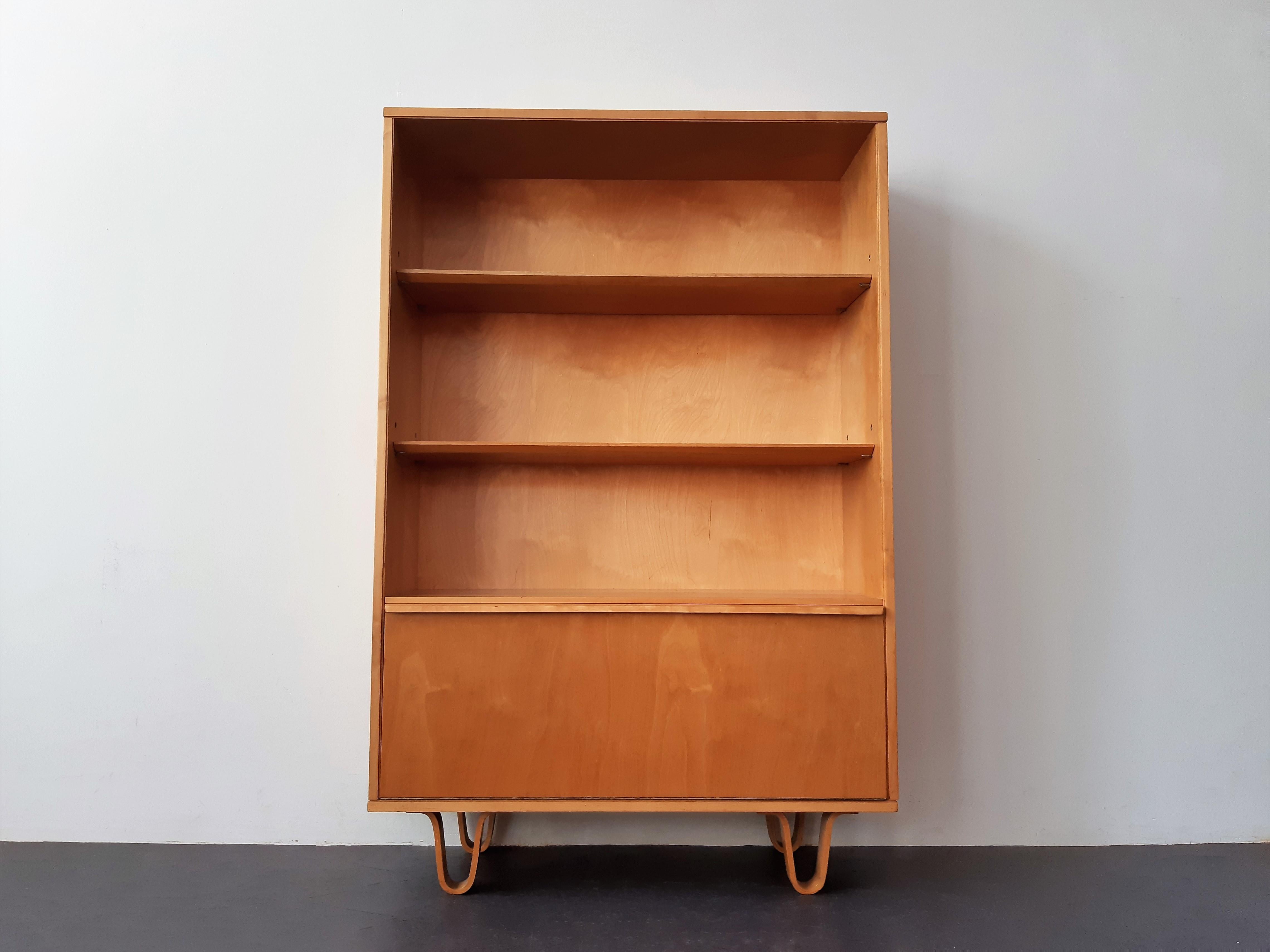 This is the BB-03 cabinet of the famous 'Birch'-series from the 1950's by Cees Braakman for Pastoe. Generally used as a bookcase. It has 2 shelves and a flap door at the bottom for storage. It has the famous bended plywood legs that give this series