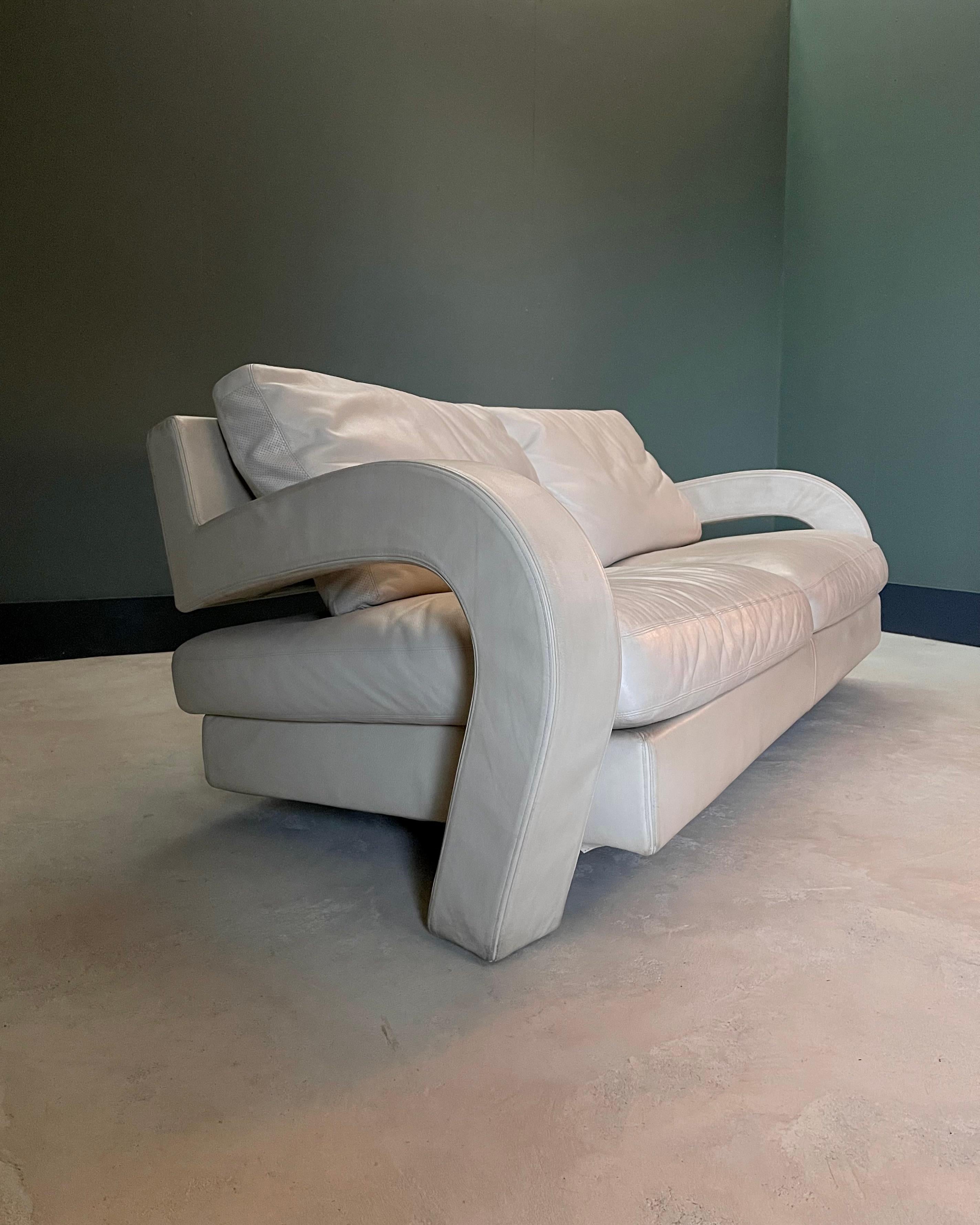 Une pièce sculpturale de B&B Italia, le canapé Balillo incarne l'élégance audacieuse du design postmoderne. Tapissée d'un cuir souple de couleur os crémeux, sa silhouette frappante est définie par des bras courbés spectaculaires qui balayent vers le