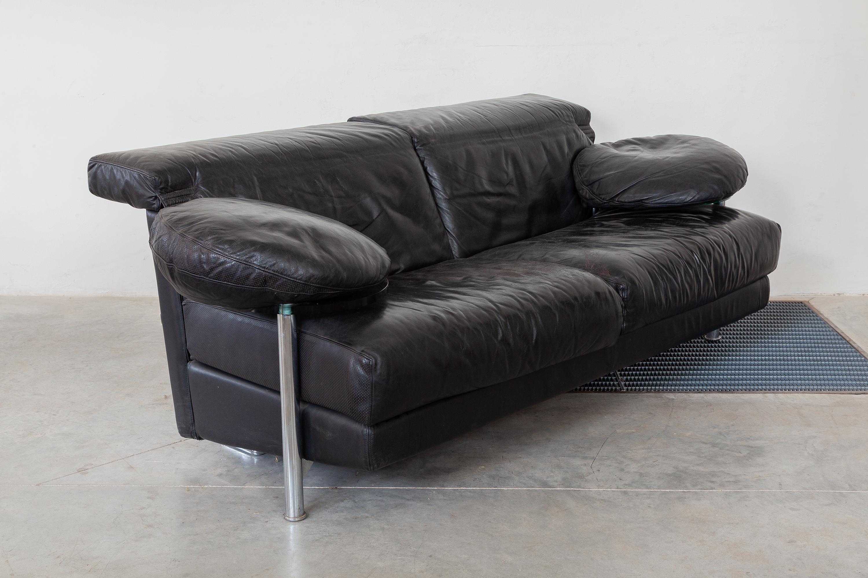 Vintage 1980s two-seat sofa by Paolo Piva for B&B Italia. Black leather upholstery with perforated accents. Circular glass side tables swivel out from under the arm rests. The back rest can be extended or folded down. Dimensions: 210 W x 88 H x 80 D