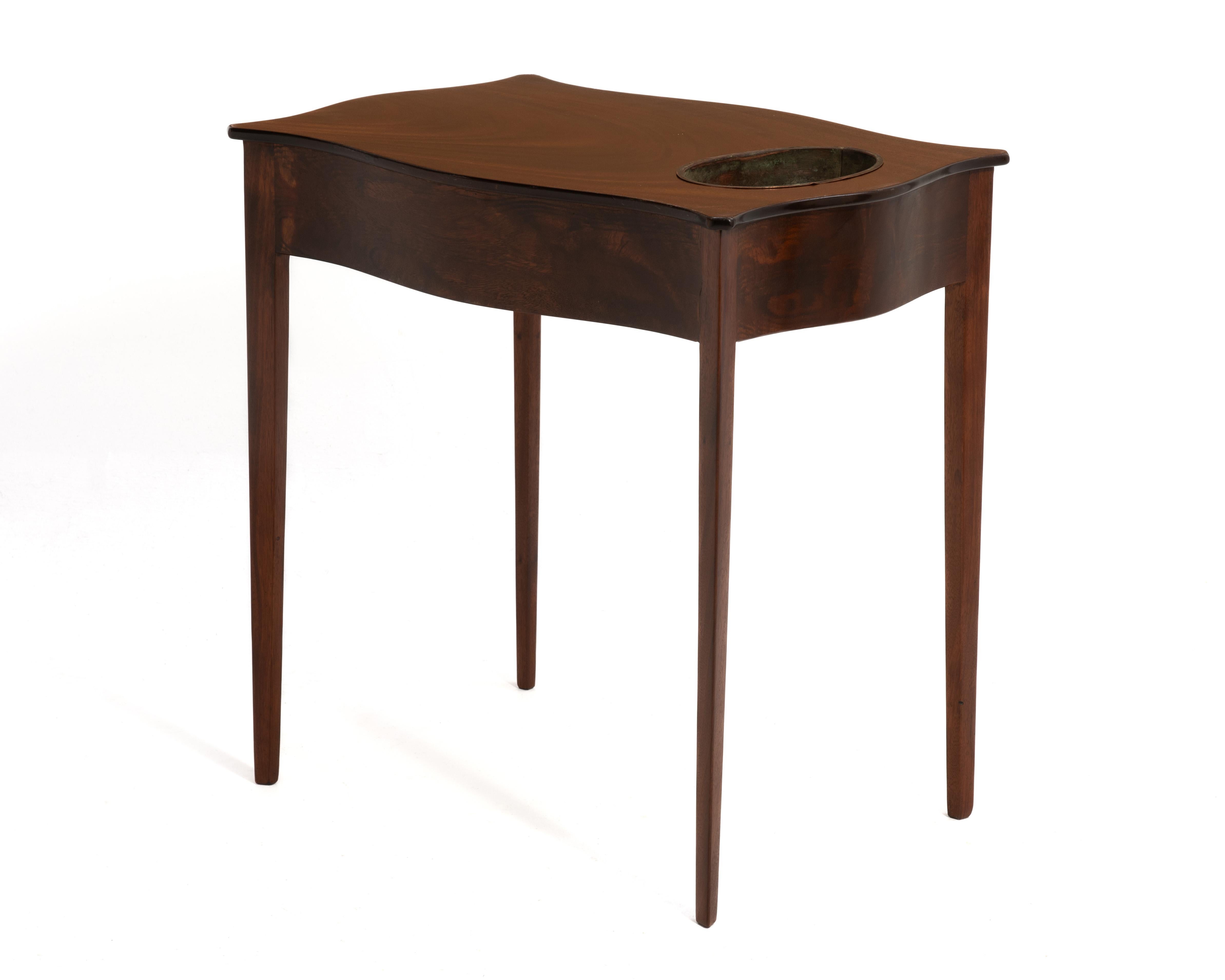 Ein Pflanzentisch aus den 1950er Jahren von Beacon Hill Collection'S. Der Tisch hat eine wunderbare, serpentinenförmige Platte aus Mahagoni-Furnier, elegante, konisch zulaufende Beine und den originalen Kupfer-Pflanzeinsatz.
Das Kupfer Pflanzgefäß