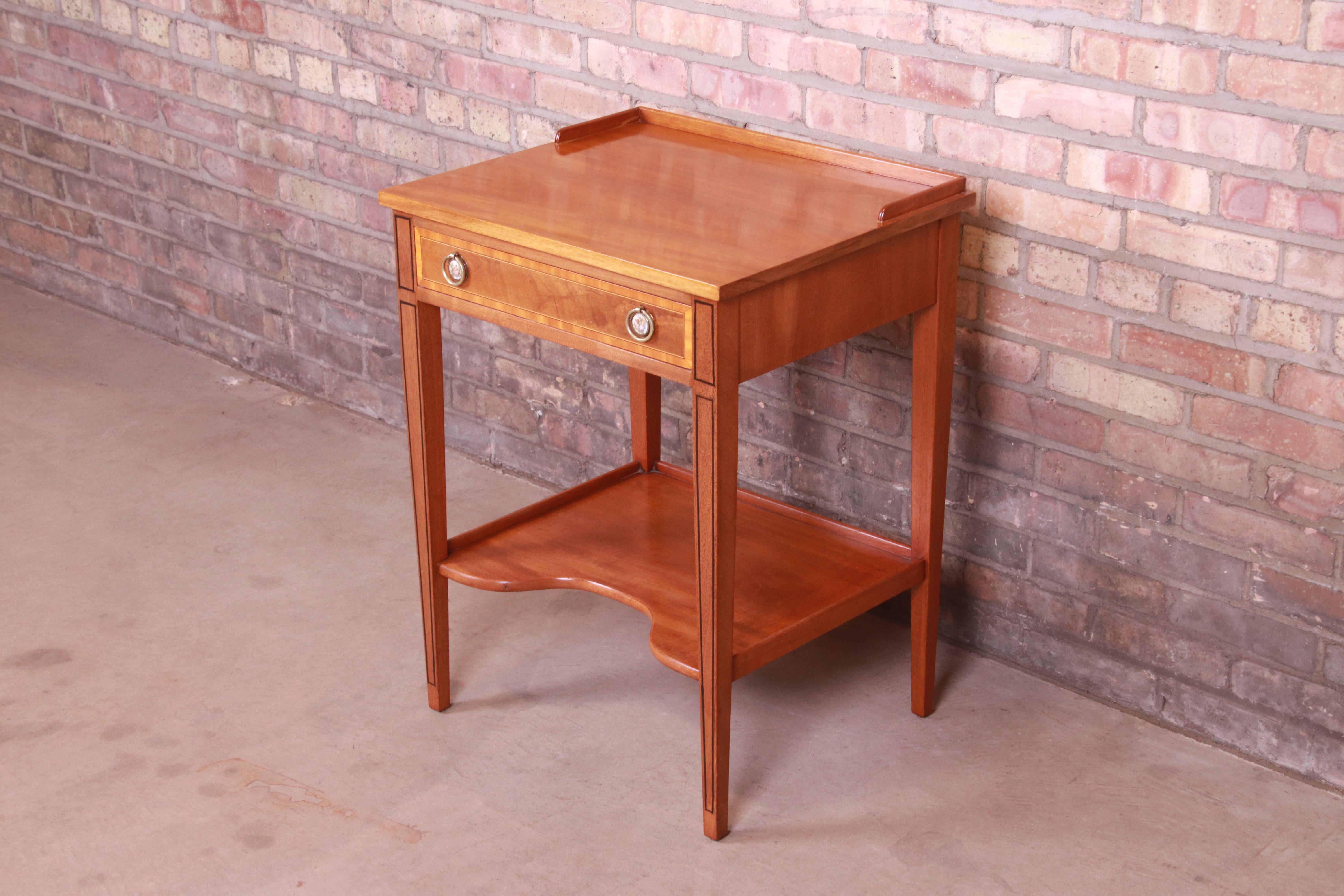 A gorgeous Federal style single drawer occasional side table or nightstand

By Beacon Hill Collection

USA, mid-20th century

Mahogany, with satinwood banding, ebonized string inlay, and unique brass and decorative porcelain