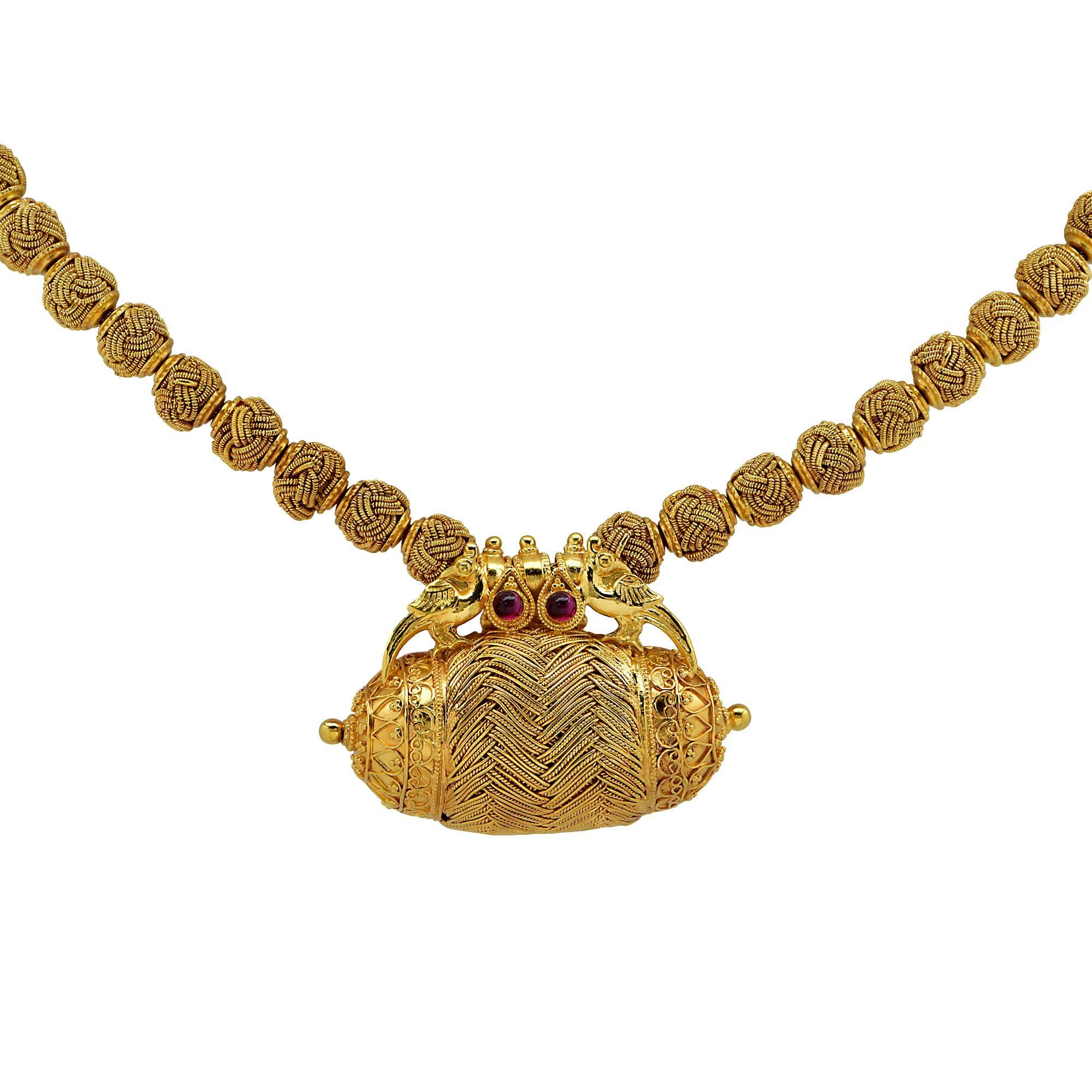 This beautifully crafted 22 karat Yellow Gold necklace boasts an amulet suspended from a 22 Karat Yellow Gold beaded necklace. Each bead is crafted with an intricate woven detail. Perched on the amulet is a pair of pheasants with two rubies resting