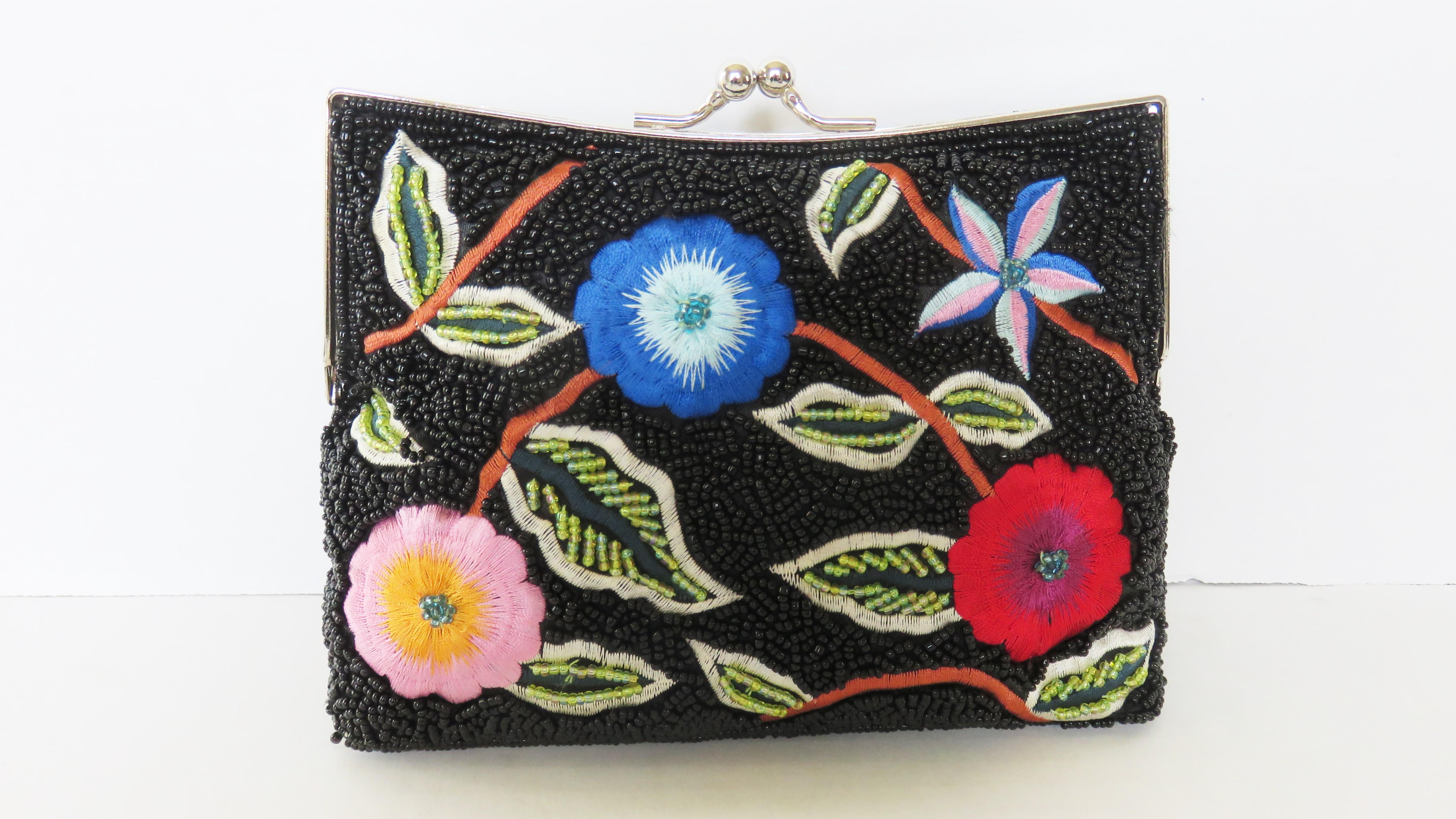 Une magnifique pochette en perles de verre noires avec des fleurs colorées brodées sur le devant et le dos.  Il est doté d'une bandoulière optionnelle en chaîne argentée qui se range dans le sac à l'aide de petites charnières afin de pouvoir