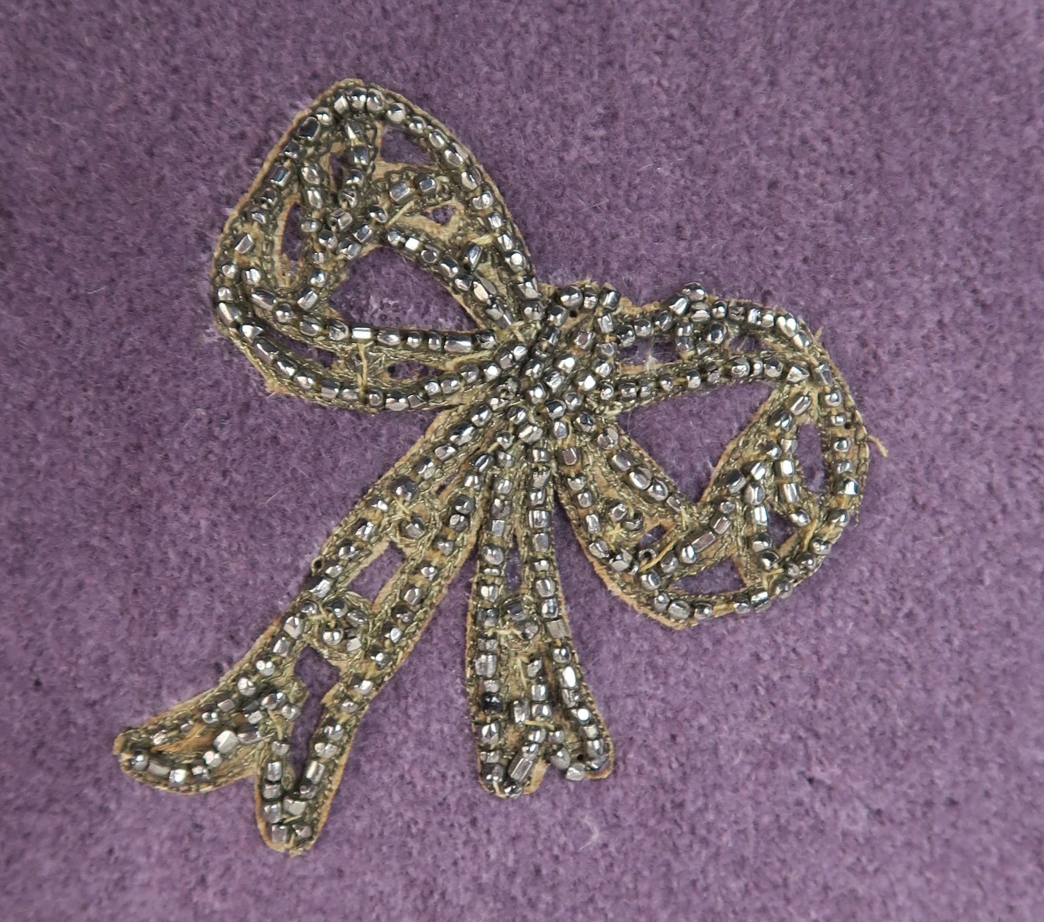 Pair of 19th century beaded bow appliqued to the corner of purple velvet pillows. Silk backs, metallic trim at sides, down inserts, zipper closures..