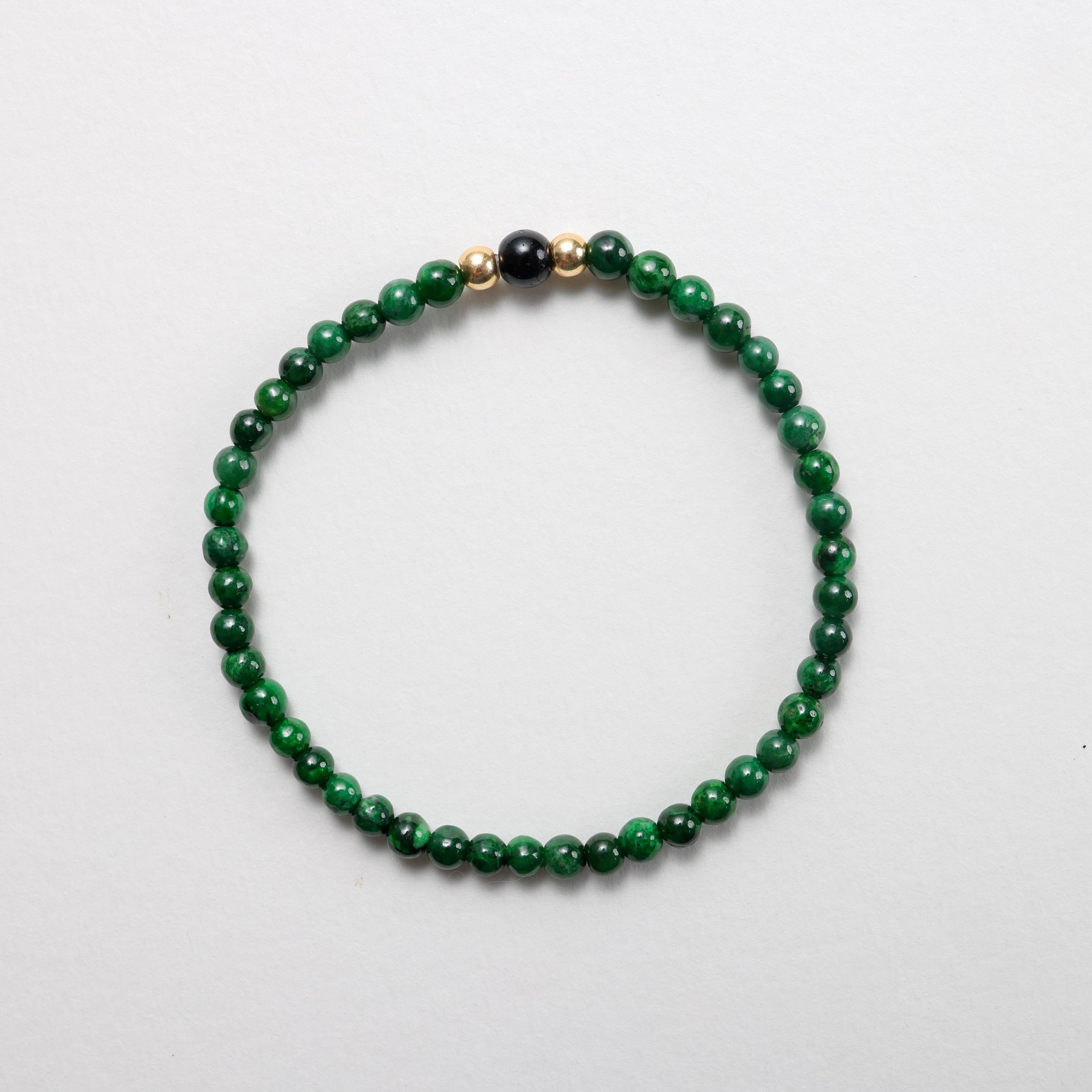 This beaded stretch bracelet features 43 incredibly rich emerald green, highly translucent natural and untreated jadeite jade beads that average 5mm in size, a pair of high-quality solid 18K yellow gold beads and a 6.51mm natural black jadeite