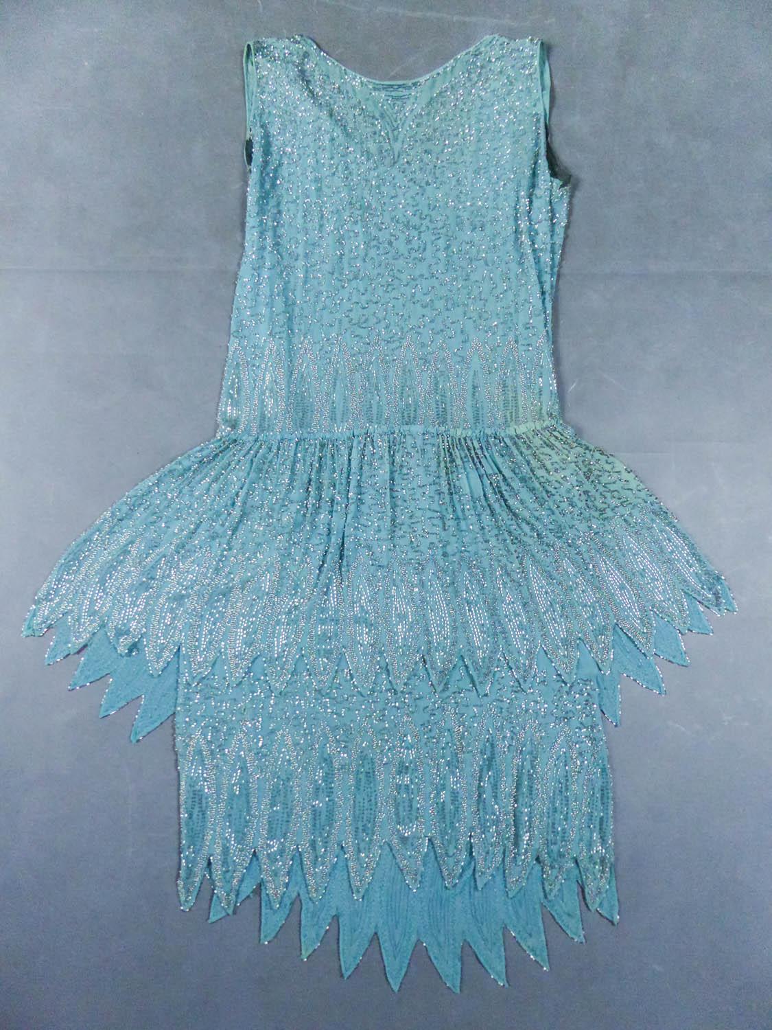 Circa 1920
France

Charleston Ball gown in turquoise silk muslin embroidered with silver tubular beads from the 1920s. Background in muslin embroidered with translucent silver and iridescent pearls in decor with vermicule. Round collar with
