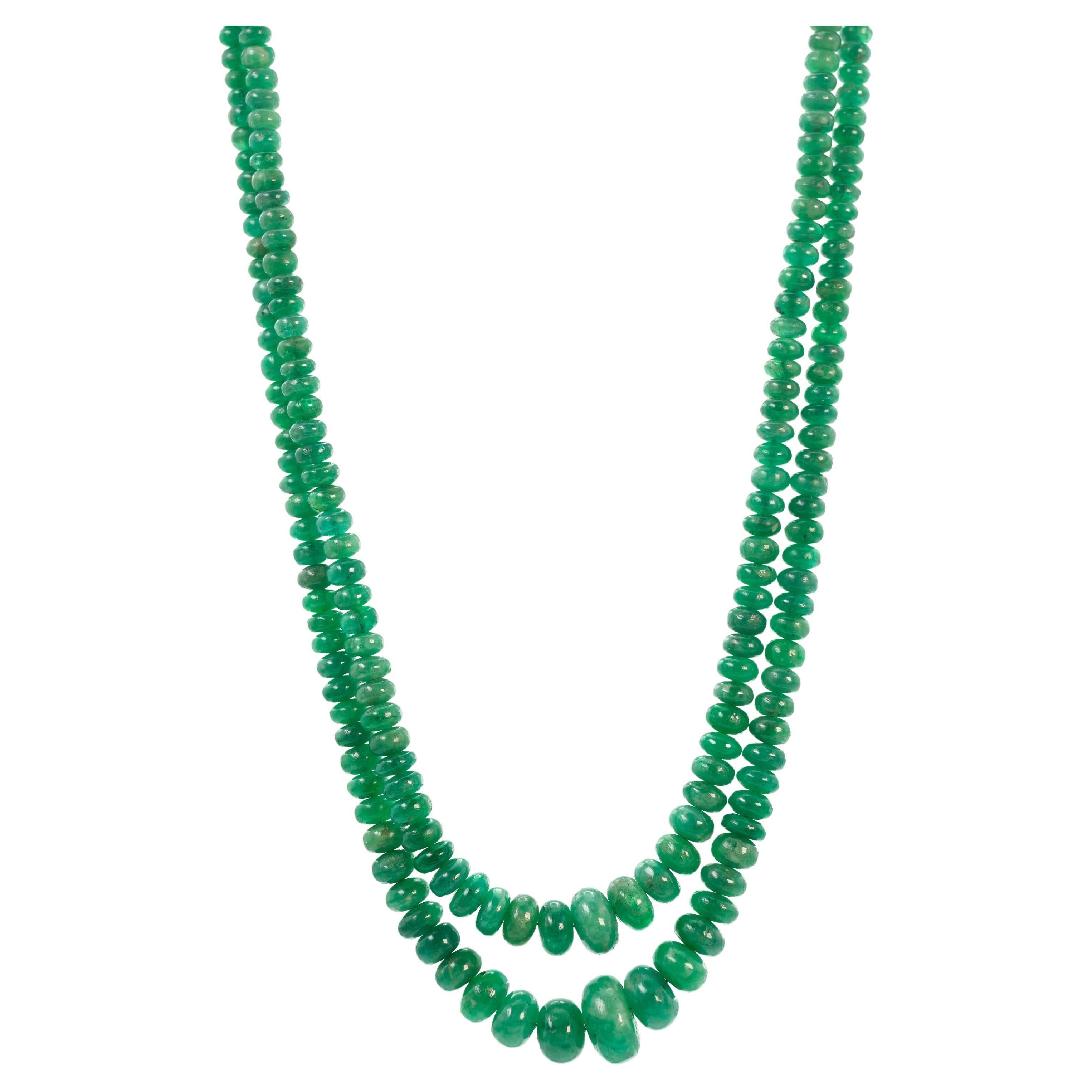 This necklace features approximately 500 emerald beads, meticulously arranged in two strands, with an estimated total weight of 125 carats. The two strands converge at a clasp accentuated by a 14 karat white gold circle pendant. The circular pendant