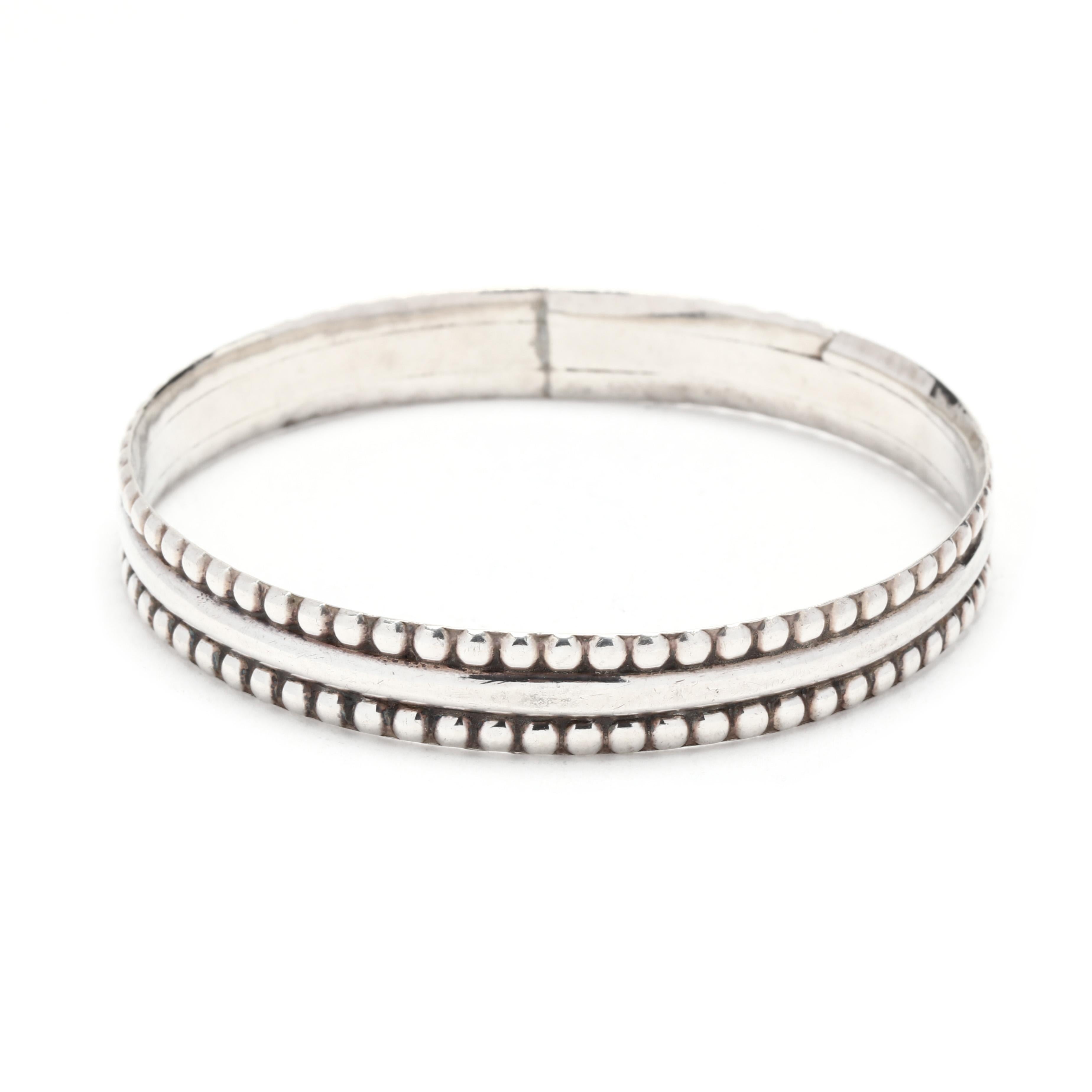 A sterling silver beaded eternity bangle bracelet.  This bangle features a smooth polished center banded with low relief beaded decoration at top and bottom edge.  It is stamped Sterling Silver and with mark SU. 

Length: 8 inches

Width: 3/8