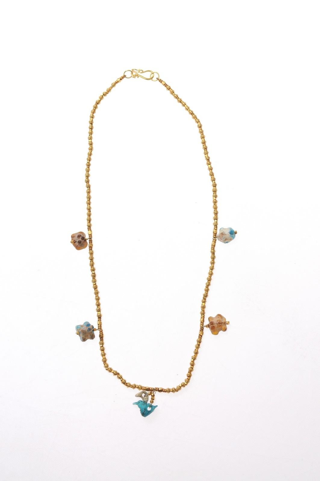 A beaded necklace with 22 karat gold beads and five ancient Roman glass fragment charms. The Roman glass fragments featured within this 22 karat gold beaded necklace are from the 1st to 3rd centuries, AD. The clasp is sturdy and features a clip to