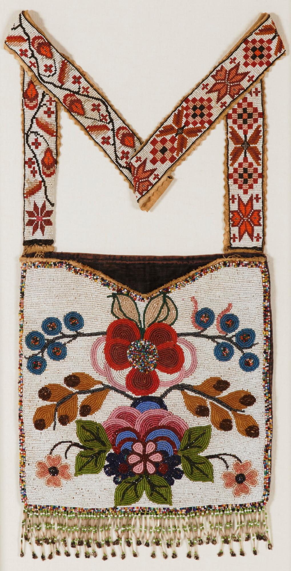 Native American bandolier bag, constructed of deer or elk hide, muslin, and velvet, with wonderful beadwork decoration. Made circa 1885, the floral imagery on the face is bold and colorful, with reds, pinks, blues, greens, brown and gold. This