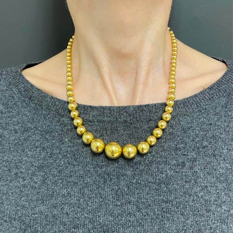 A beaded necklace of French origin, made of 18k gold. The necklace has a clean look with a graduated arrangement of high polished gold spheres. The design follows a smooth progression, starting with smaller beads at the clasp and gradually